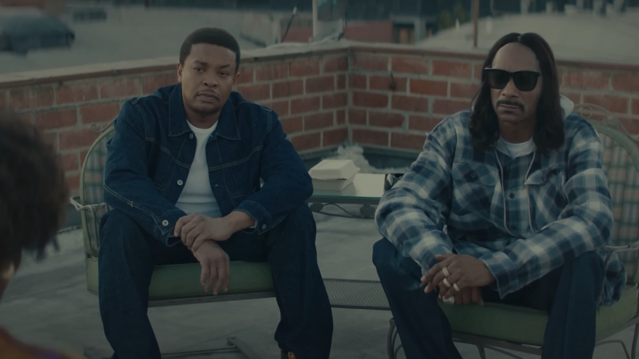Dr. Dre and Snoop Dogg sit on a rooftop. Snoop Dogg is wearing sunglasses and a plaid shirt.