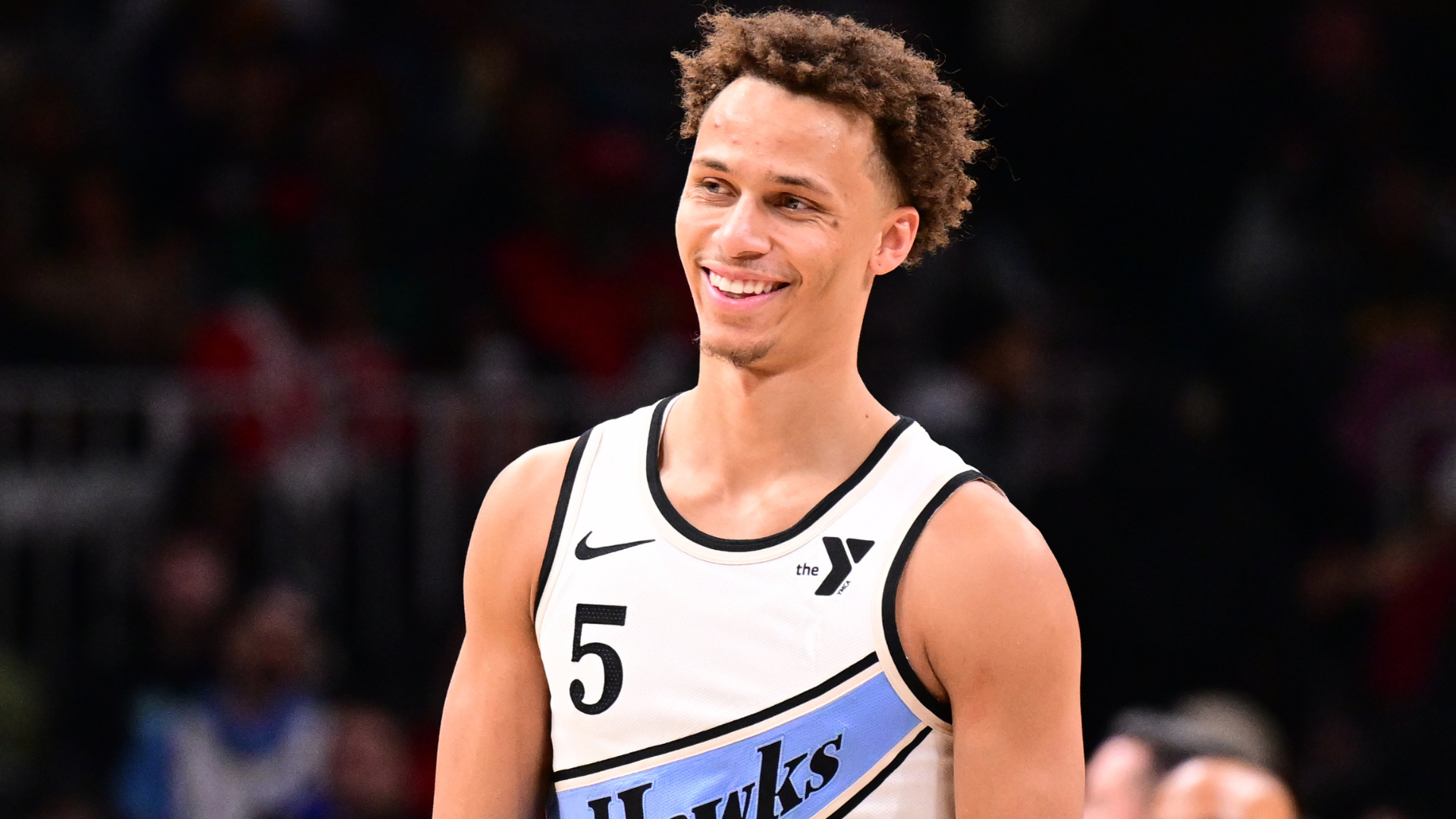 A basketball player wearing a Hawks jersey with the number 5 smiles on the court.