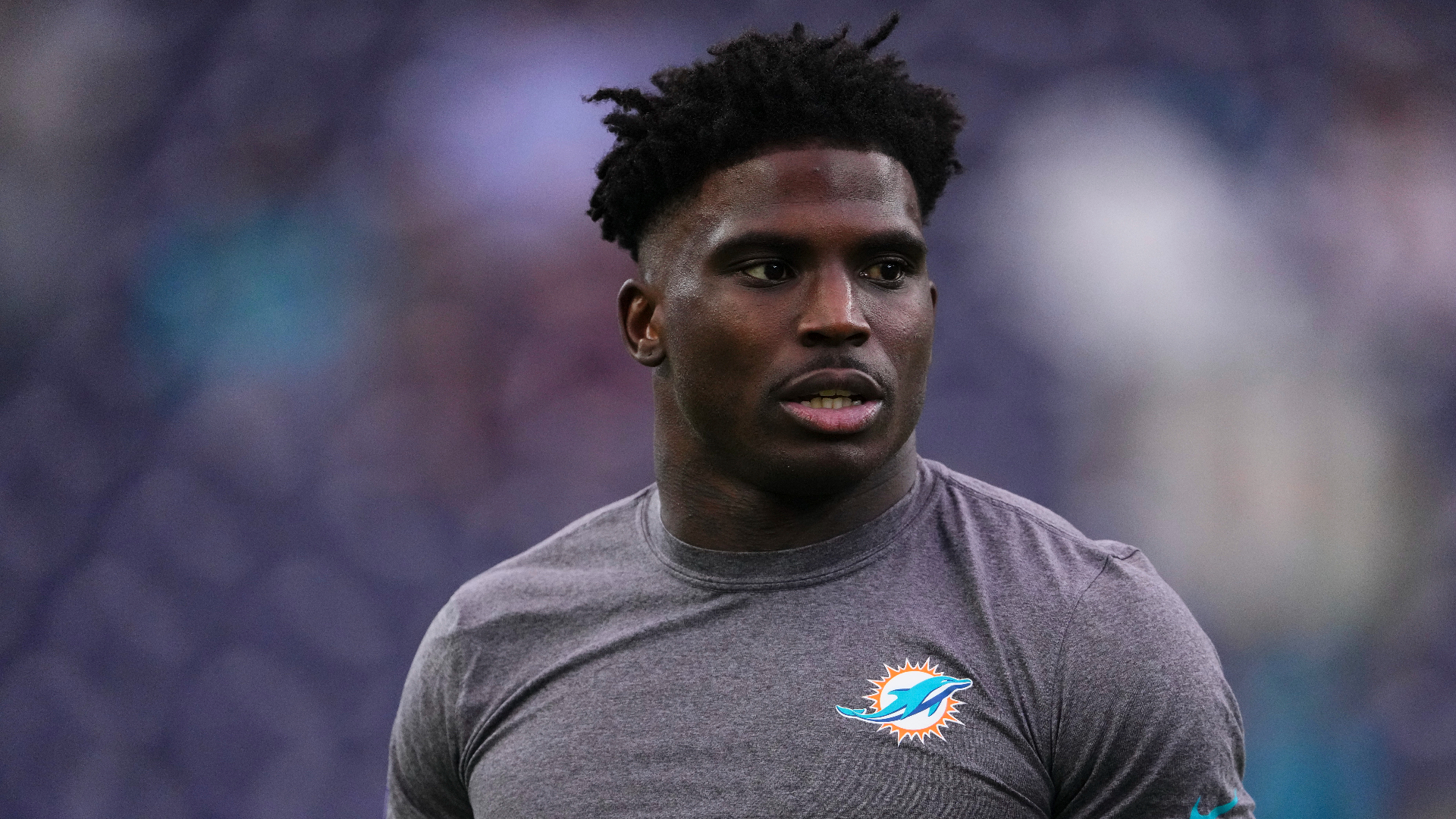 Tyreek Hill wearing a Miami Dolphins shirt while standing on a football field.