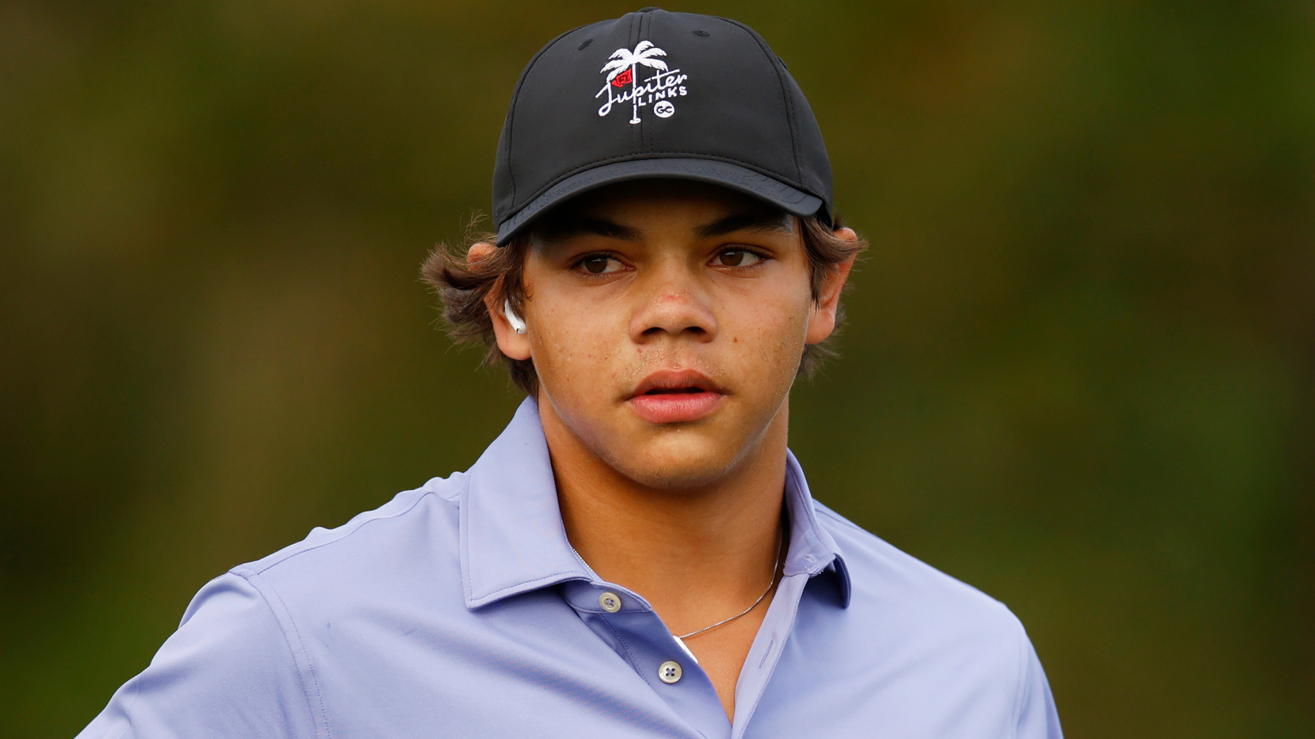 Young man wearing a black cap and a light purple collared shirt, looking to the side.
