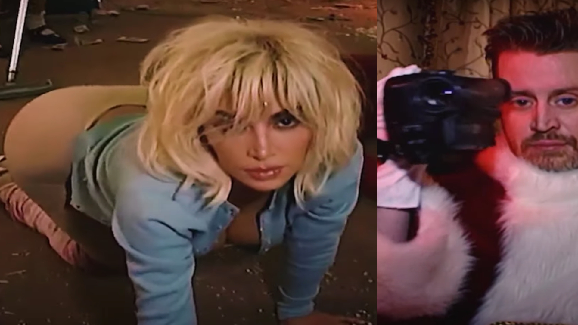 A woman with blonde hair kneels on the floor, wearing a blue top. Beside her, a man in a fur outfit holds a camera.