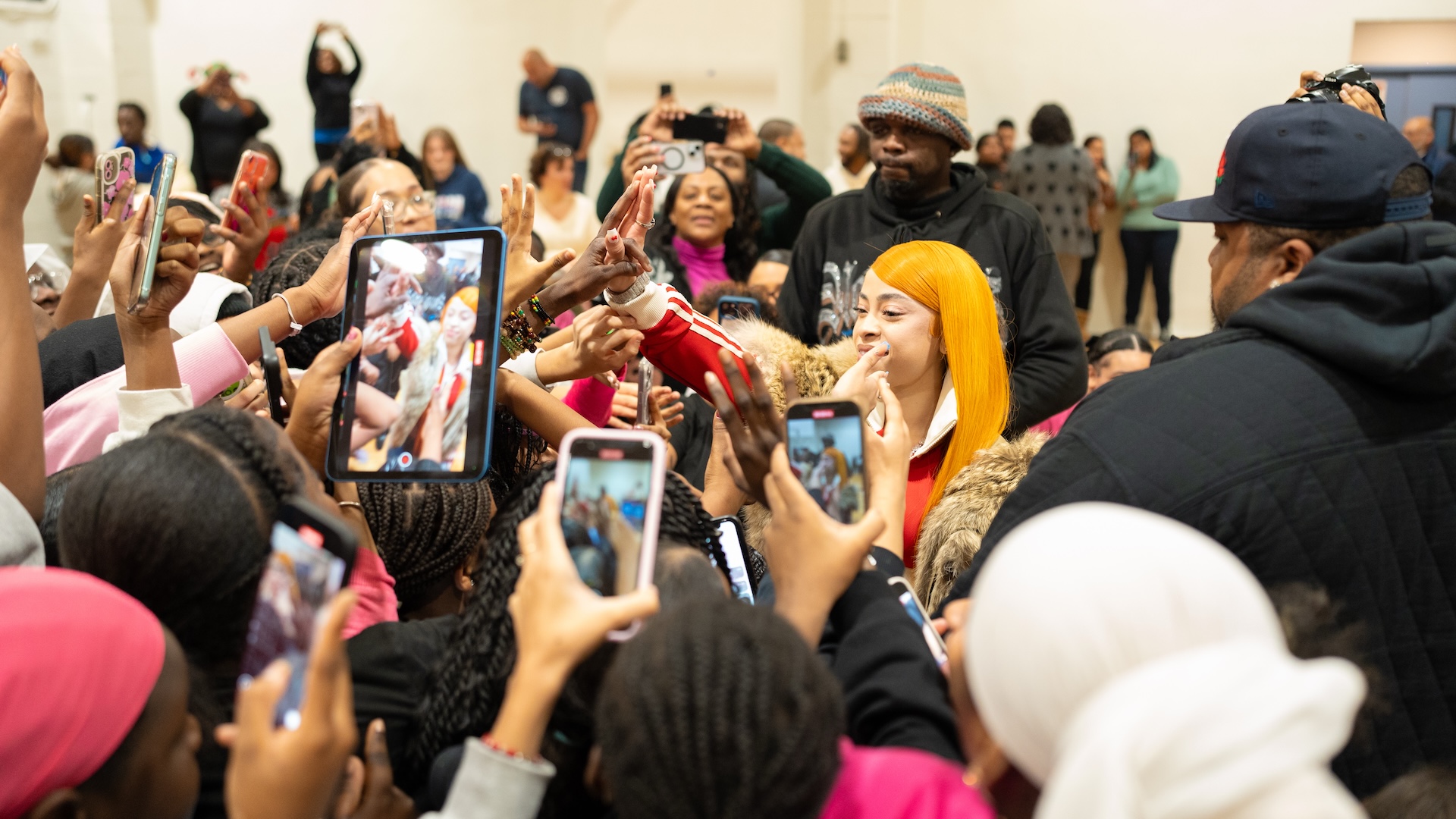A crowd of people surrounds Ice Spice, taking photos and reaching out to her.