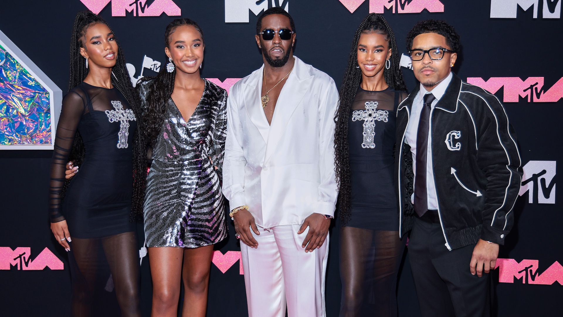 Sean "Diddy" Combs in a white suit with four others at the MTV event. The group poses in front of a black and pink MTV backdrop.