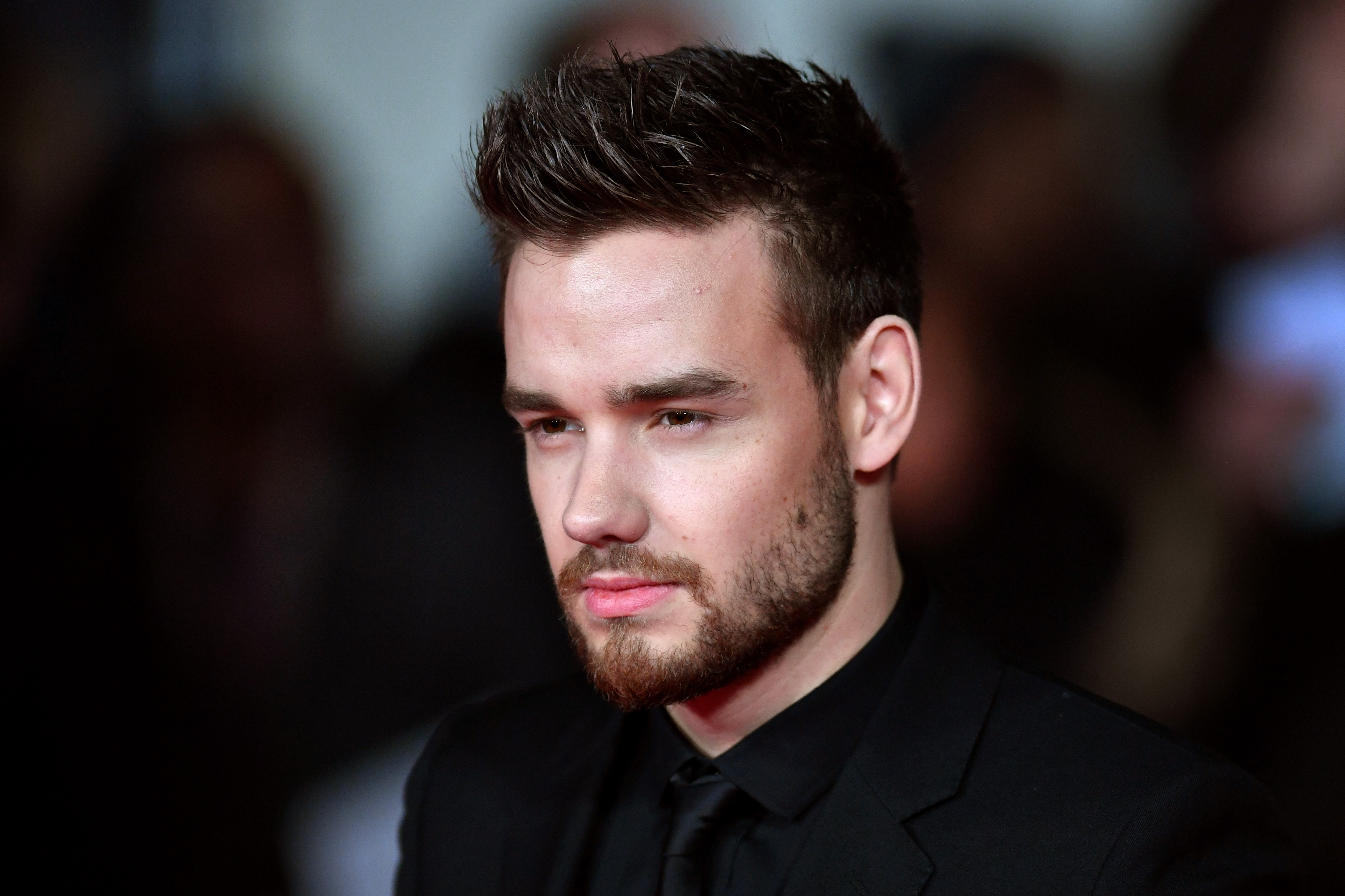 Liam Payne in a black suit, with styled hair and a beard, at a formal event.