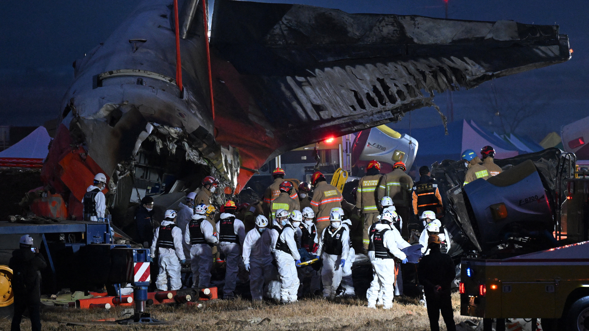 Emergency responders at a nighttime scene of a plane crash, with damaged aircraft parts and rescue personnel in protective gear.