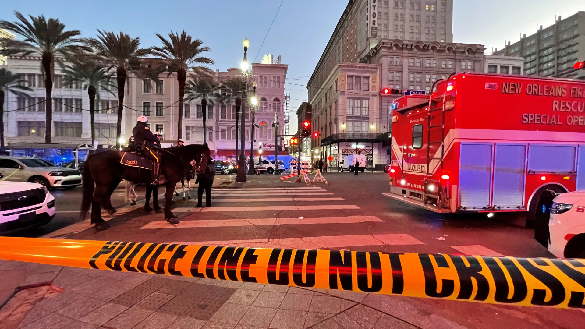 A city street scene with police tape, mounted police officers, and a fire rescue vehicle in New Orleans.