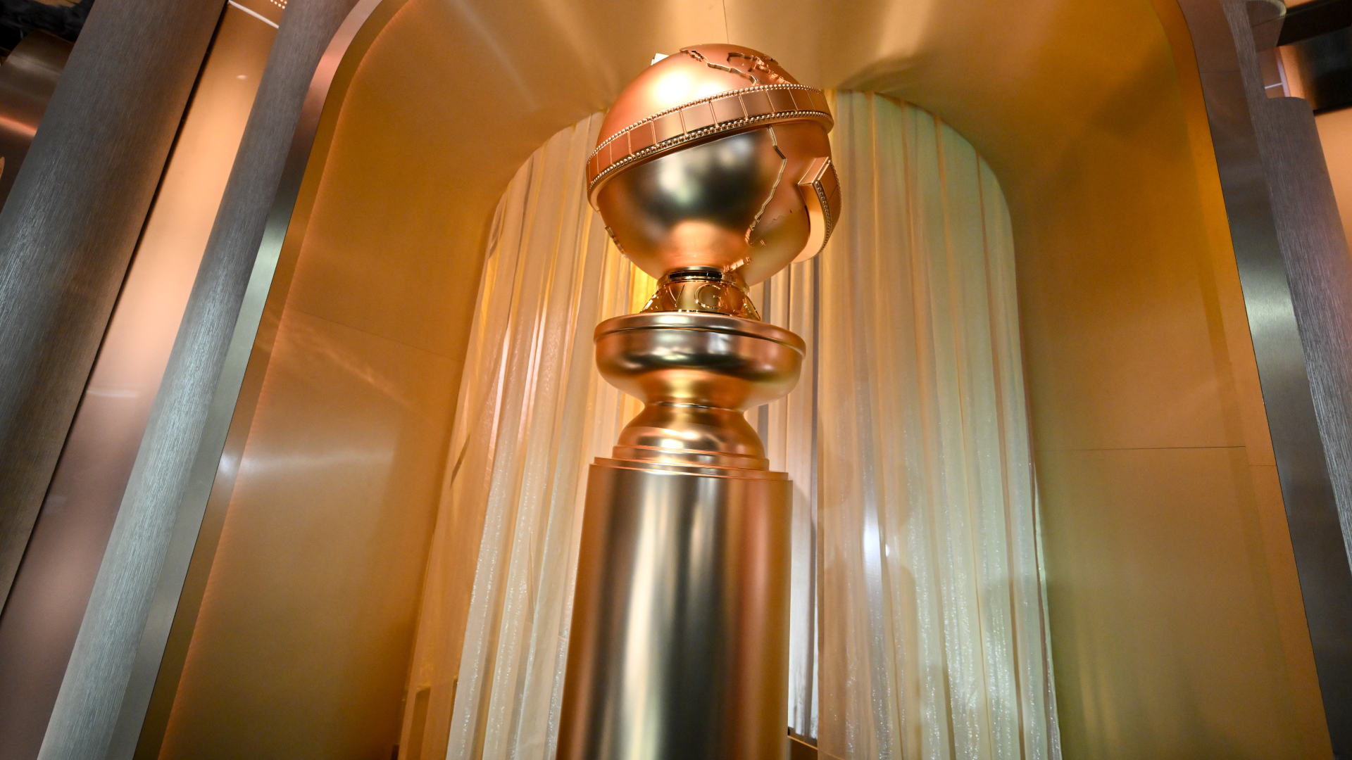 A large Golden Globe award statue displayed in a shiny, golden setting with draped curtains in the background.