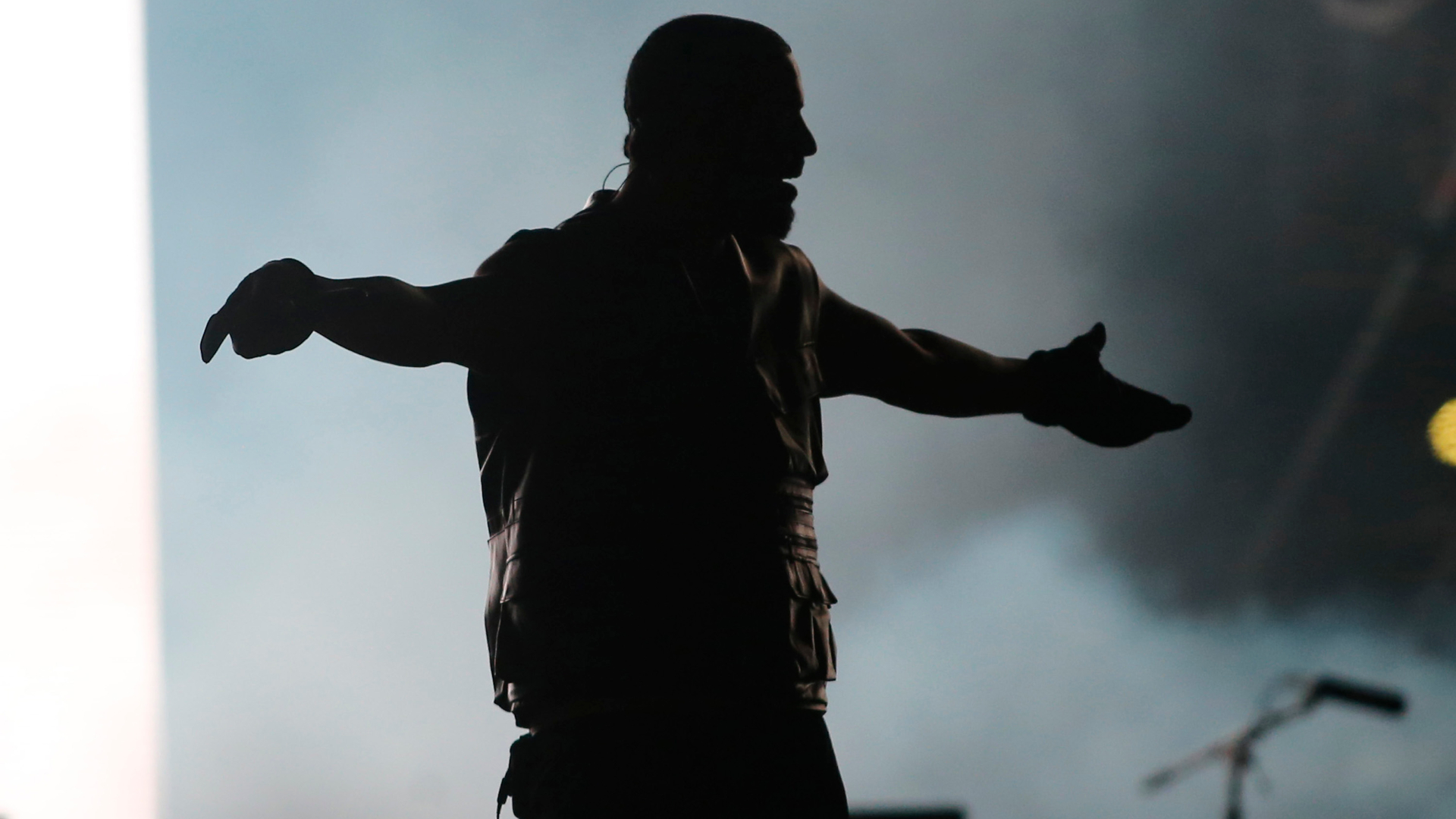 Silhouette of a person on stage with arms outstretched, against a smoky, illuminated background.