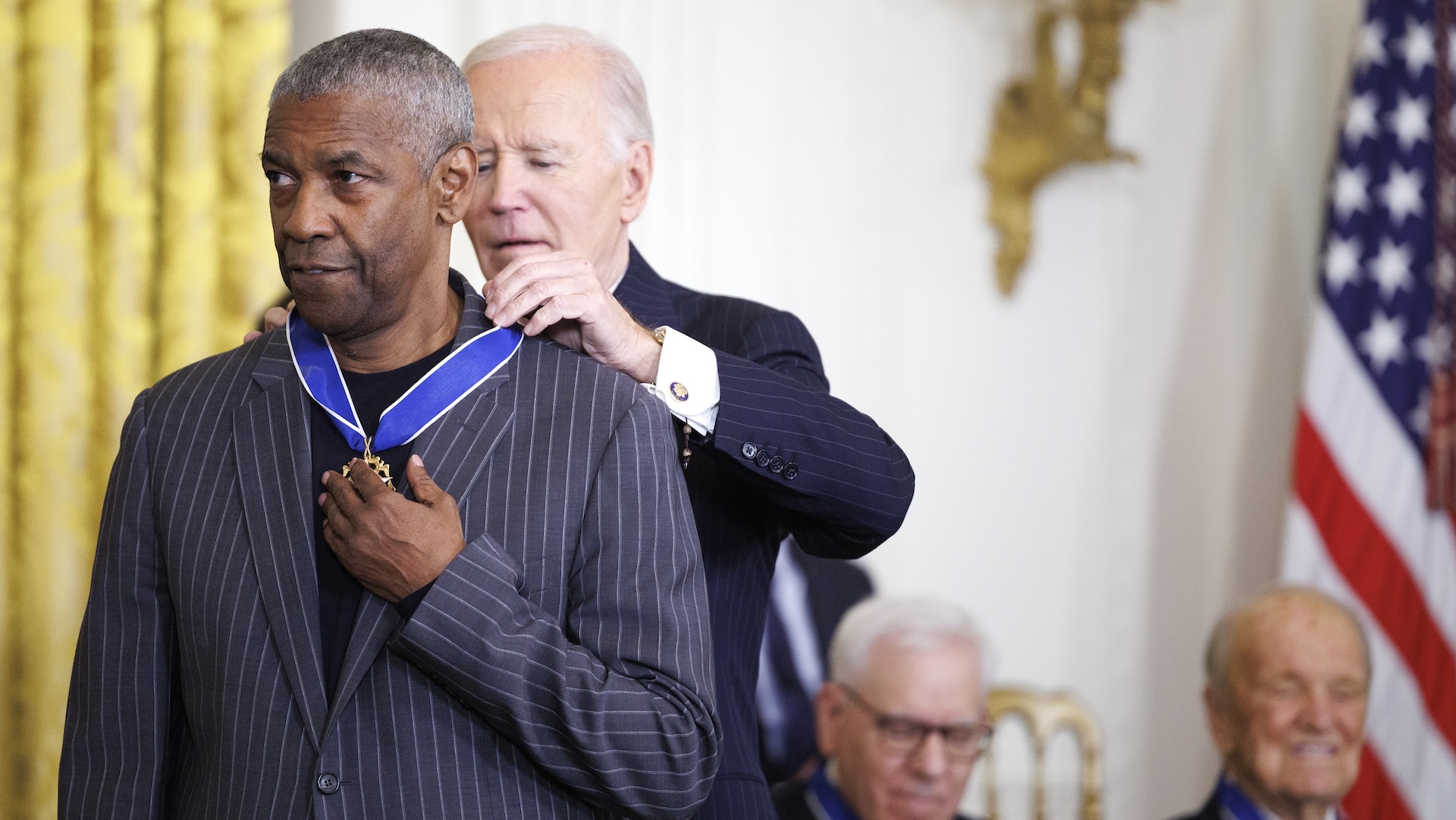 President Joe Biden awards Denzel Washington the Presidential Medal of Freedom. Other recipients are seated in the background.