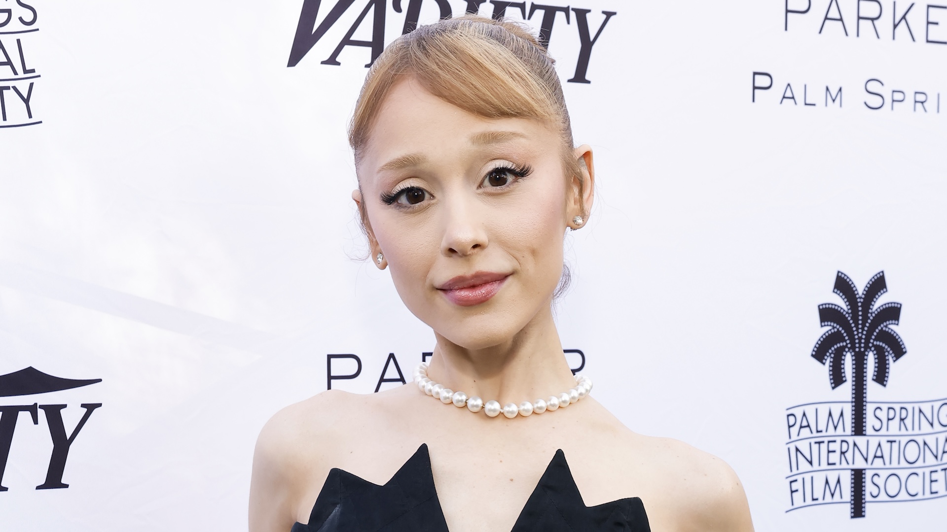 Ariana Grande wearing pearls against a backdrop for the Palm Springs International Film Society. 