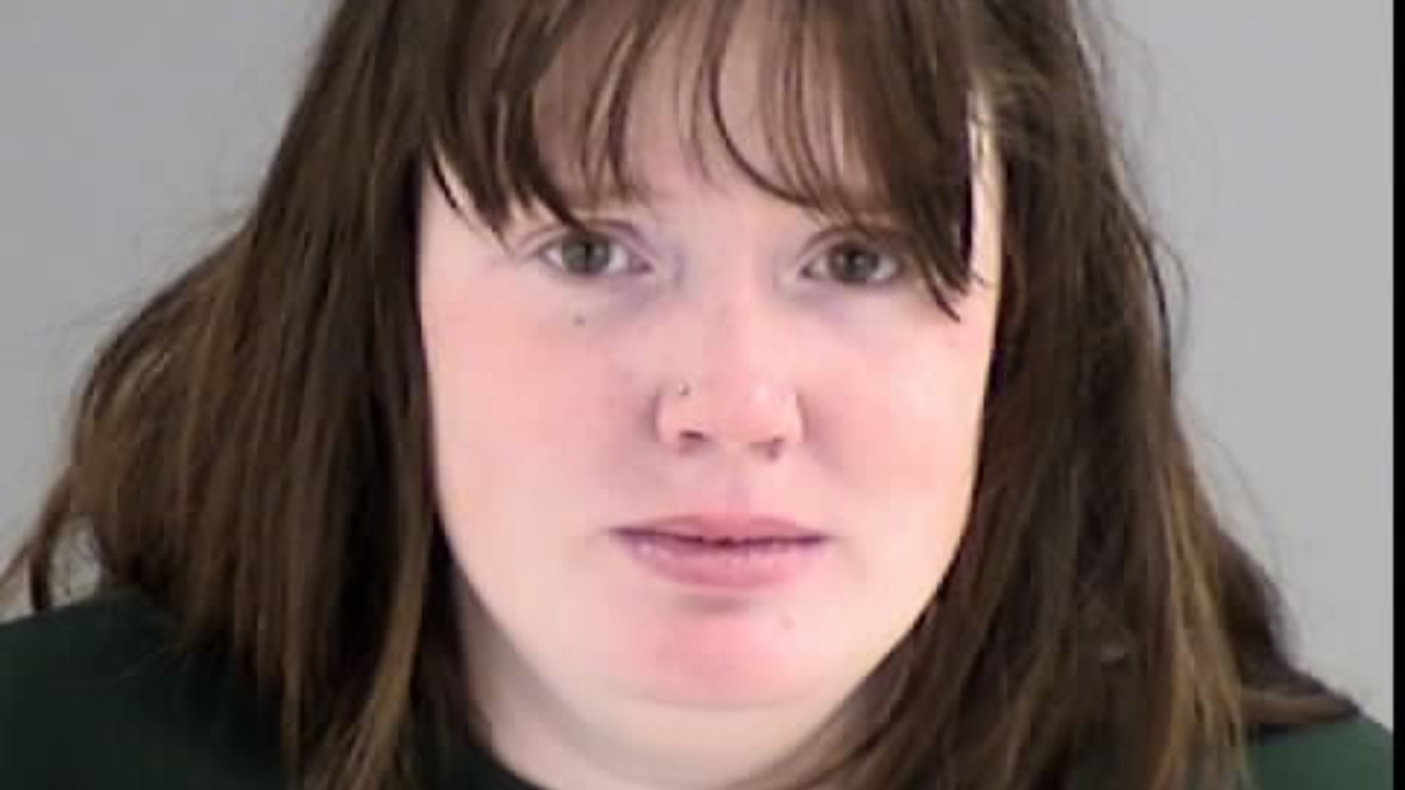 A woman with long brown hair, wearing a dark top, looking directly at the camera.