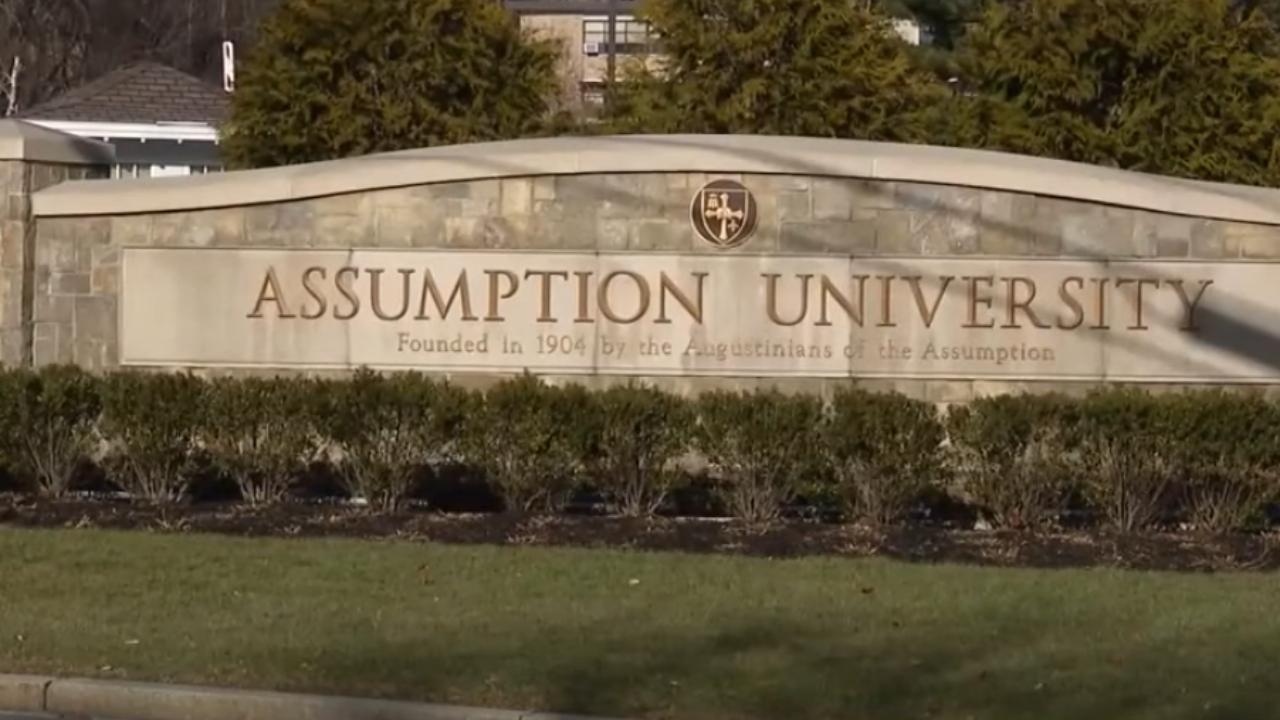 Sign for Assumption University, founded in 1904, with greenery and trees in the background.