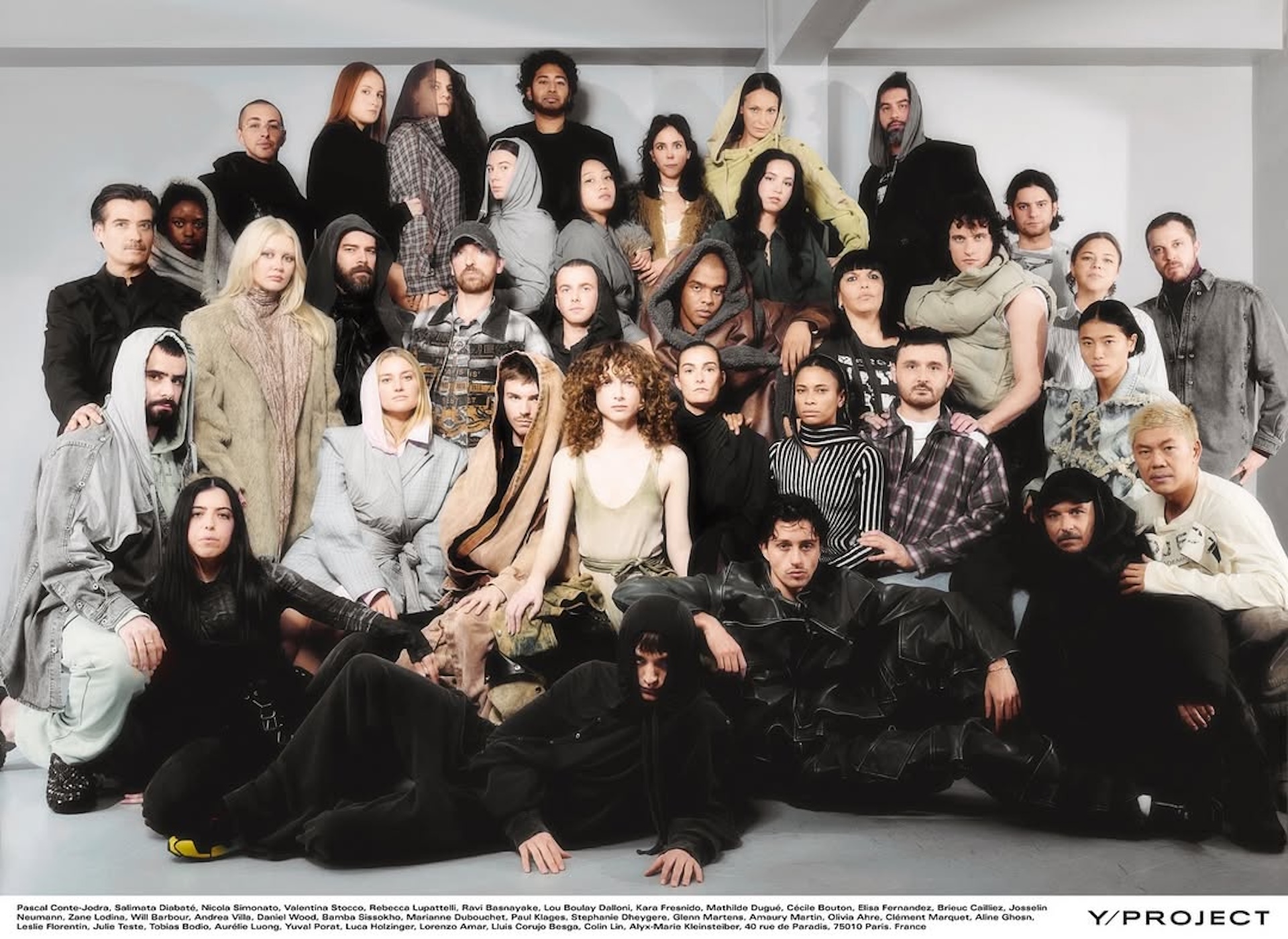 A diverse group of models in various stylish outfits pose together in a studio setting for Y/Project.