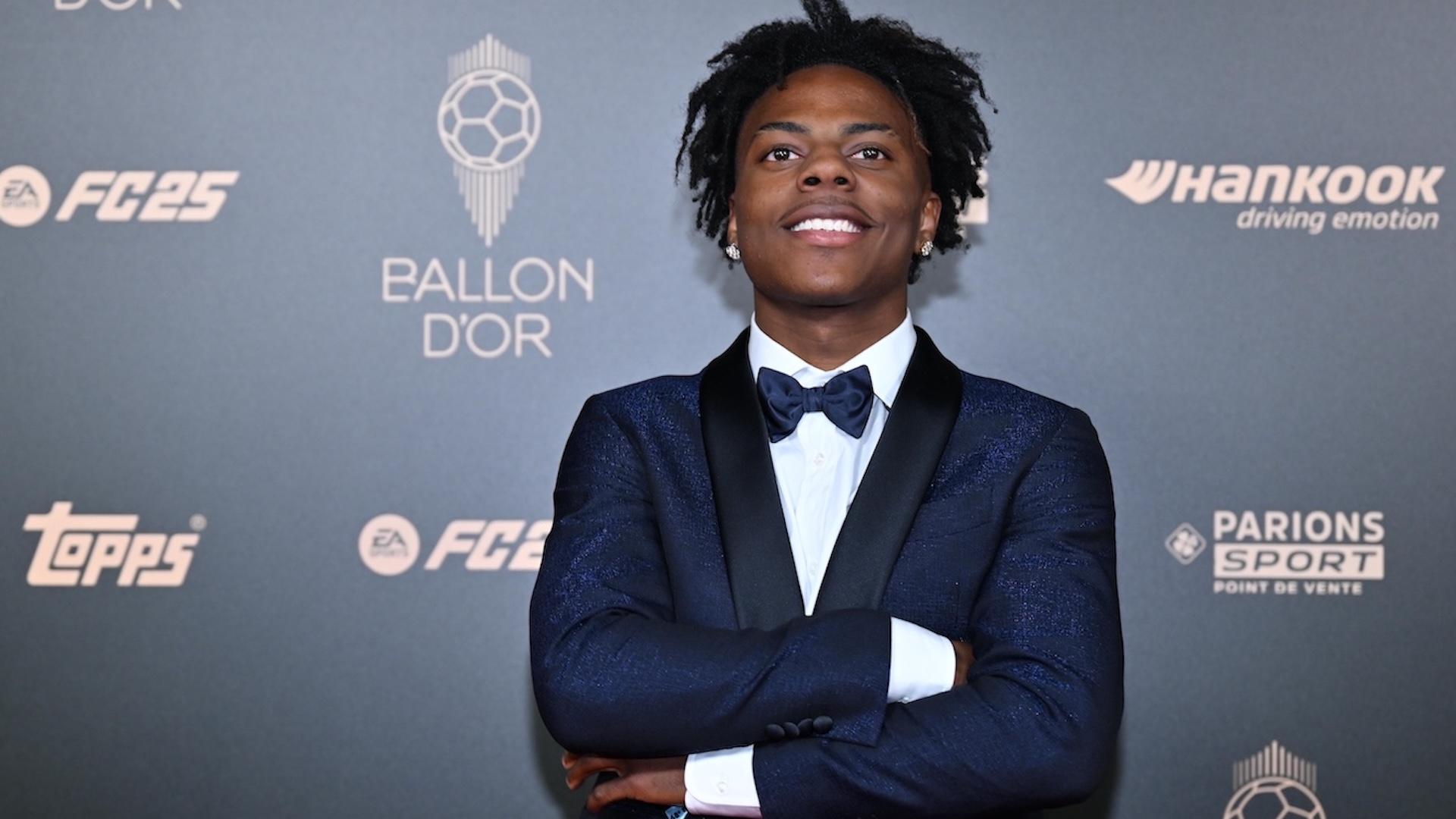 iShowSpeed in a blue tuxedo with a bow tie stands confidently at the Ballon d'Or event backdrop.