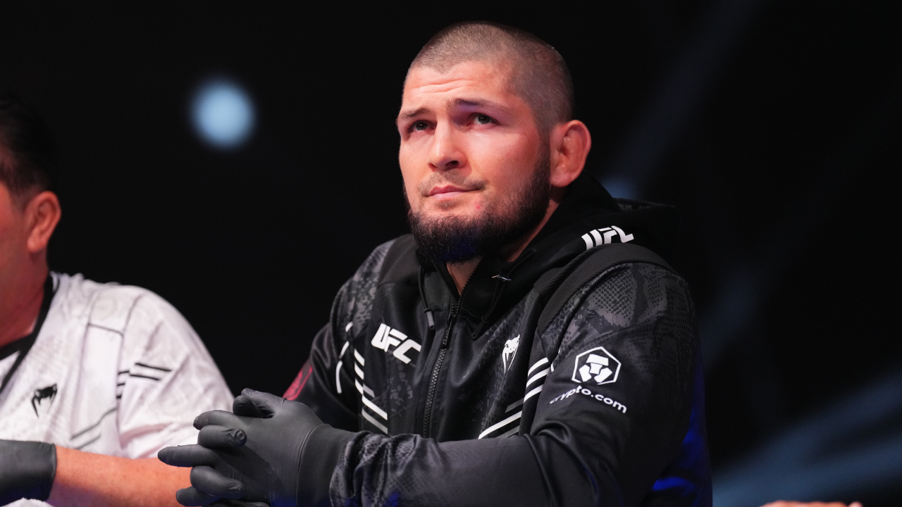 Khabib Nurmagomedov, wearing a black UFC jacket, sits at a table with a thoughtful expression.