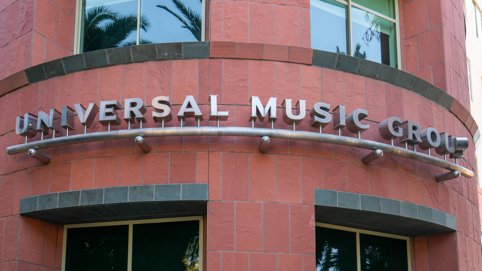 Sign on a red brick building reads "Universal Music Group," with windows and palm tree reflections visible.