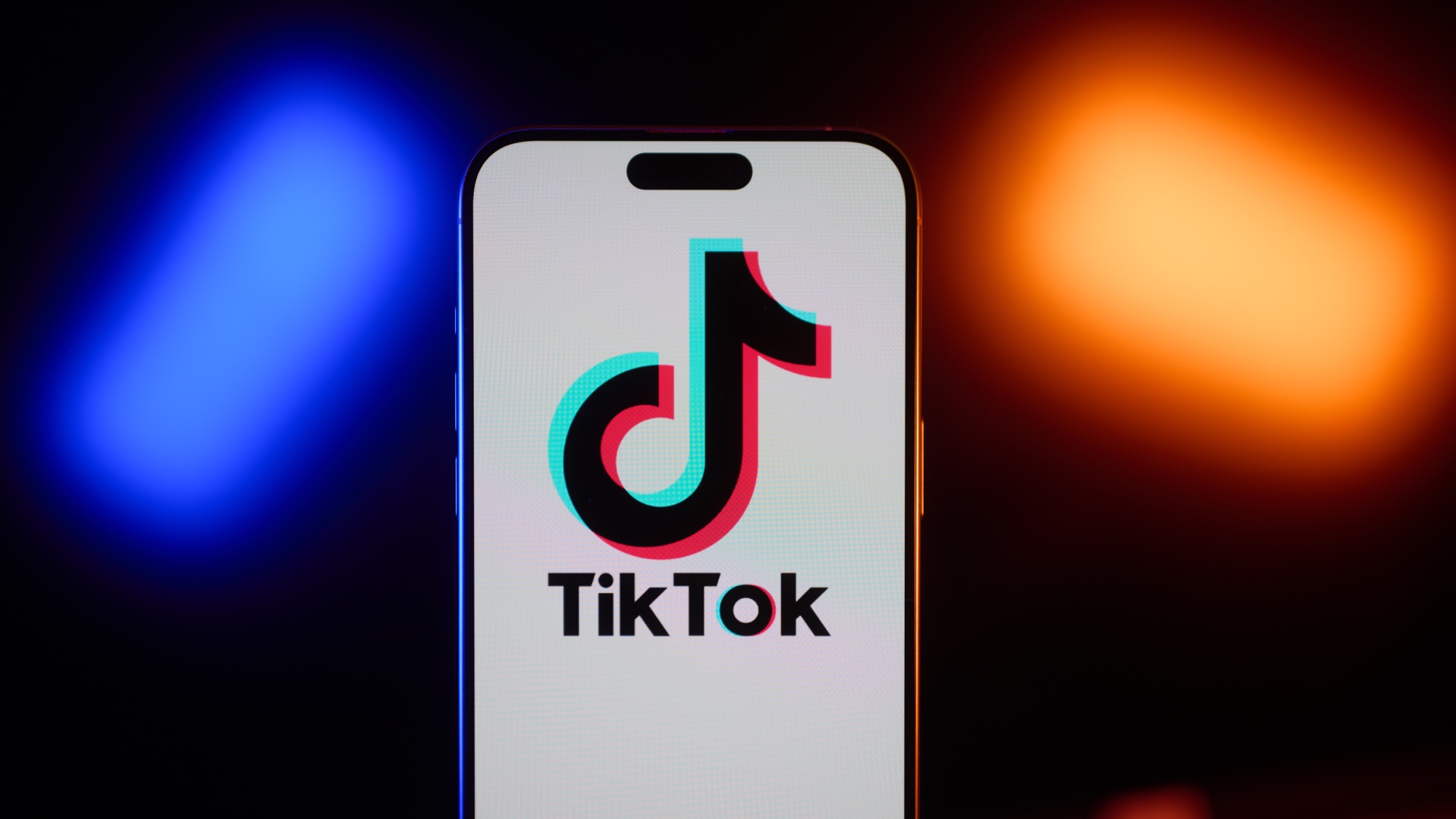 Flanked between blue and orange lights, an iPhone displays the TikTok app's logo.