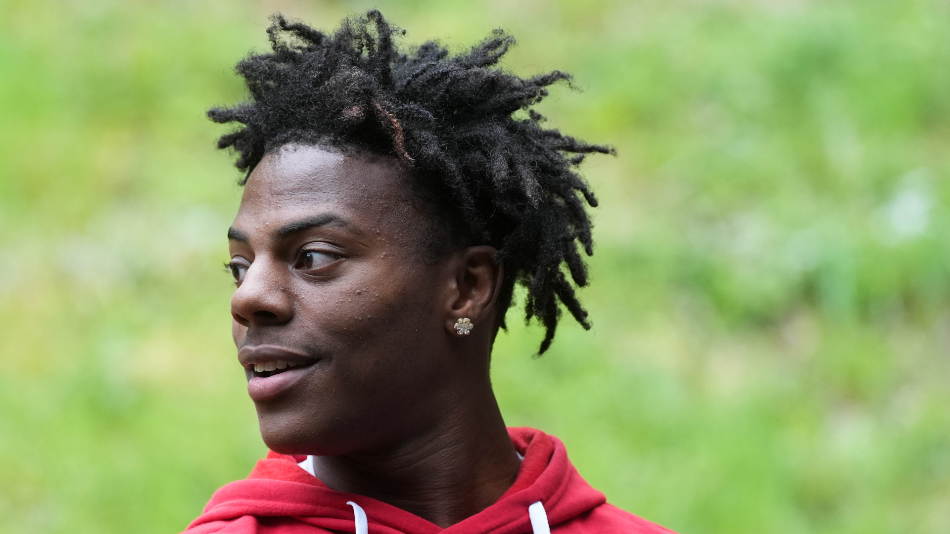 Speed wearing a red hoodie, looking to the side, with a grassy background.