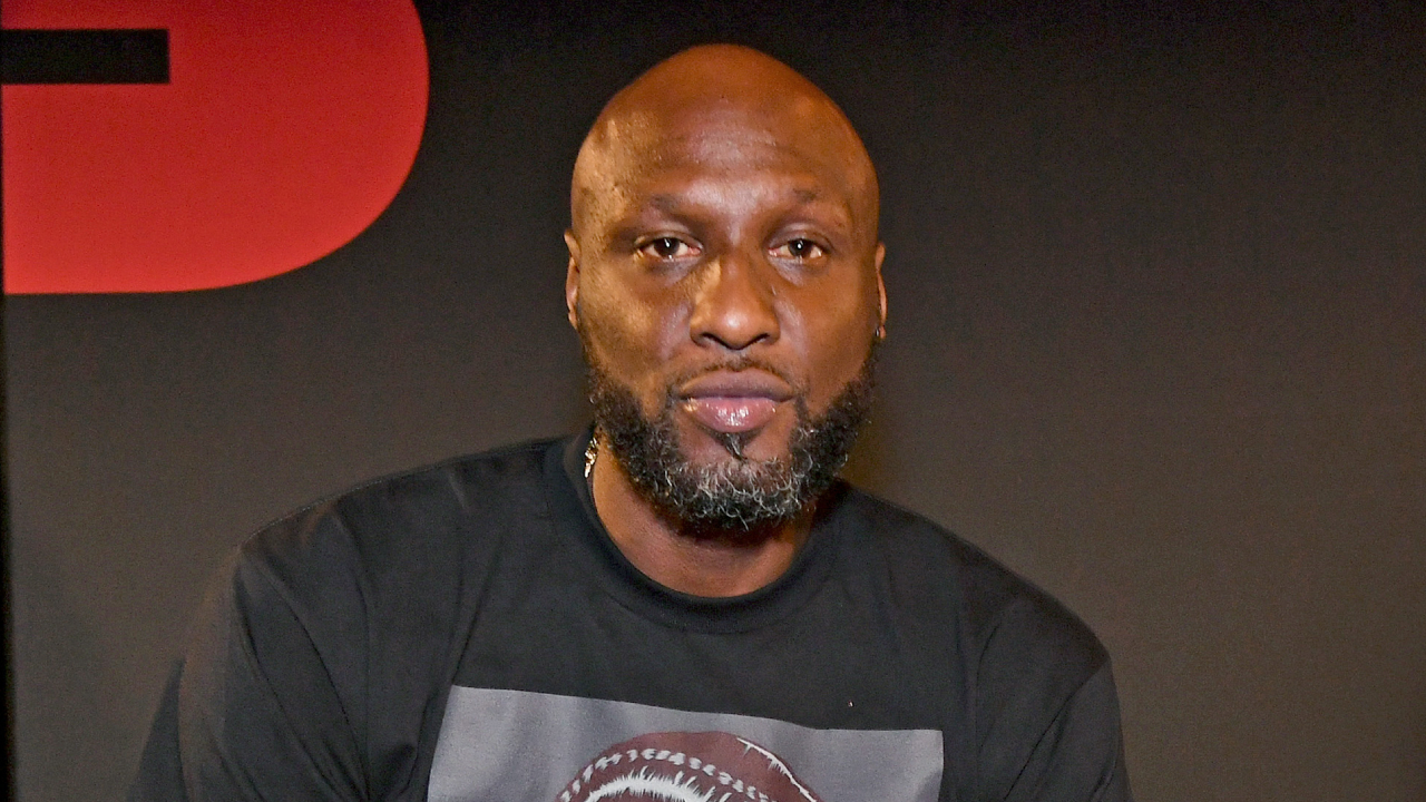 Lamar Odom, wearing a black t-shirt, is seated against a dark background.