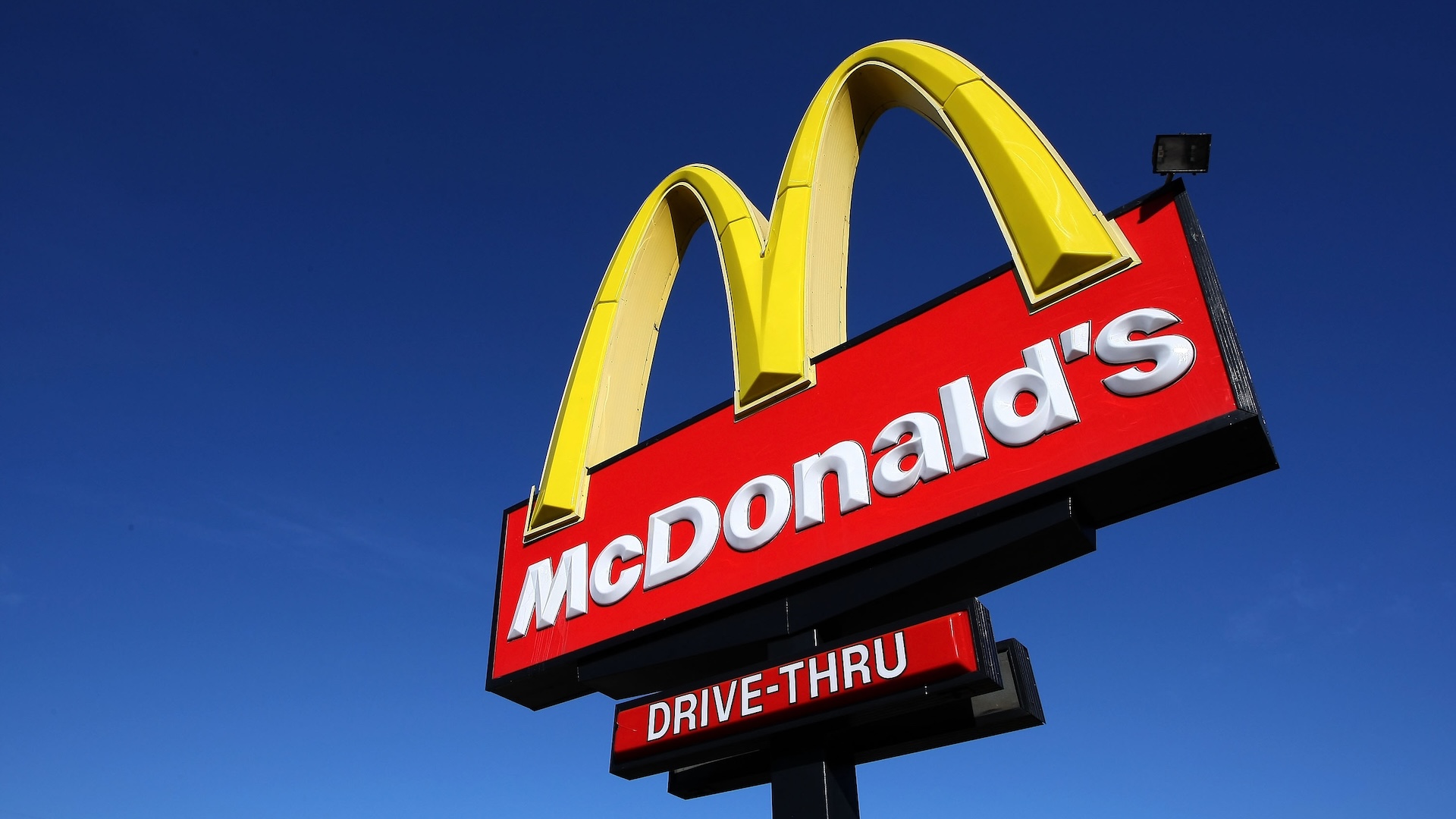 A McDonald's drive-thru sign with the iconic yellow arches against a clear blue sky.