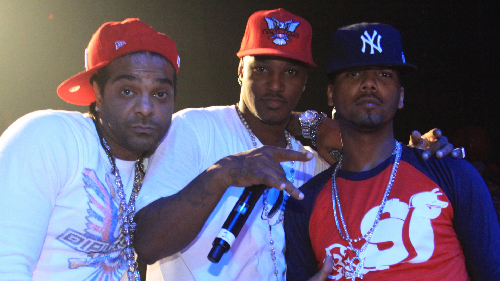 Three men wearing baseball caps and chains, posing together on stage.