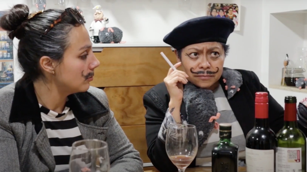 Two people dressed as stereotypical French characters with berets and drawn mustaches, sitting at a table with wine bottles and glasses.