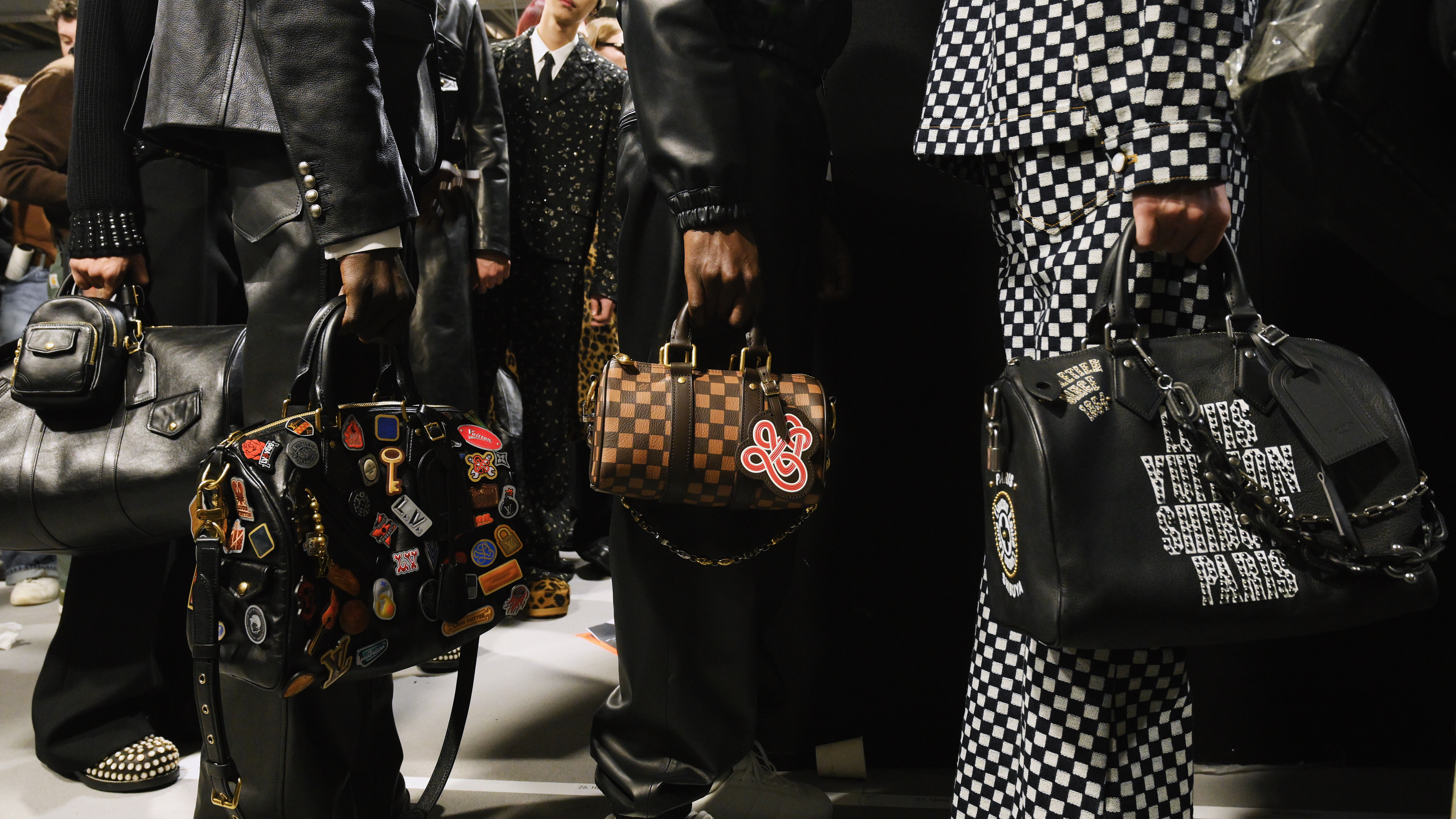 Fashionable individuals holding designer handbags, wearing patterned and leather outfits. The bags feature various designs and embellishments.