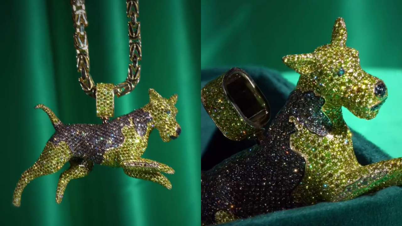 A jeweled dog pendant, adorned with green and brown stones, displayed on a green fabric background.