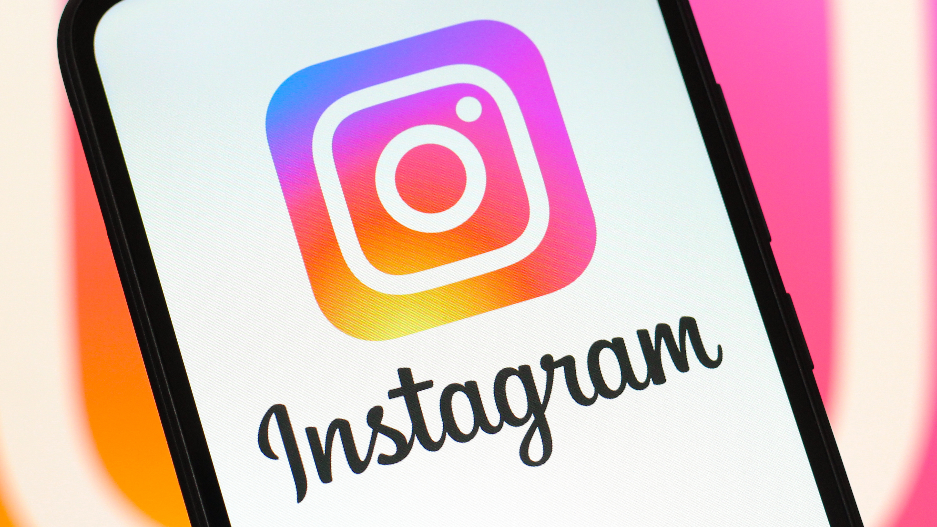 A smartphone screen displaying the Instagram logo and text, with a blurred Instagram logo in the background.