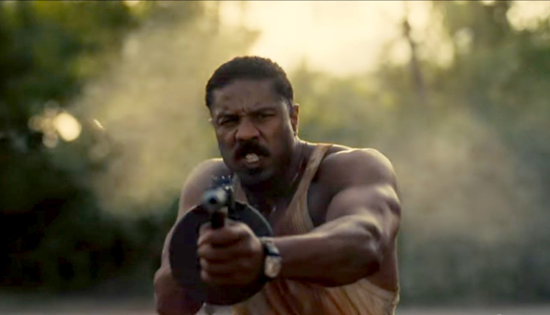Michael B. Jordan grimaces while firing a gun at the screen.