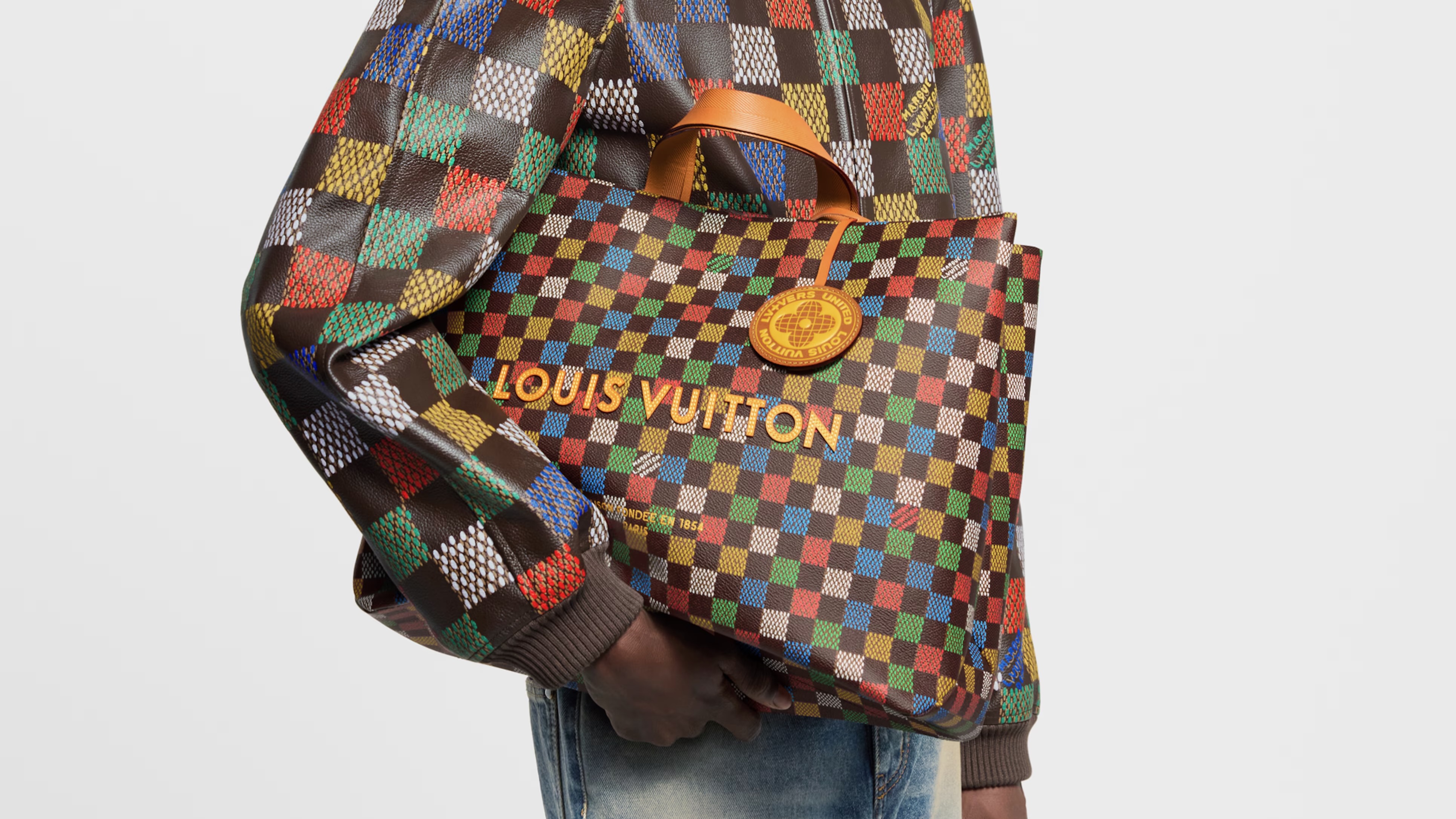 Person holding a colorful checkered Louis Vuitton bag, wearing a matching patterned jacket and jeans.