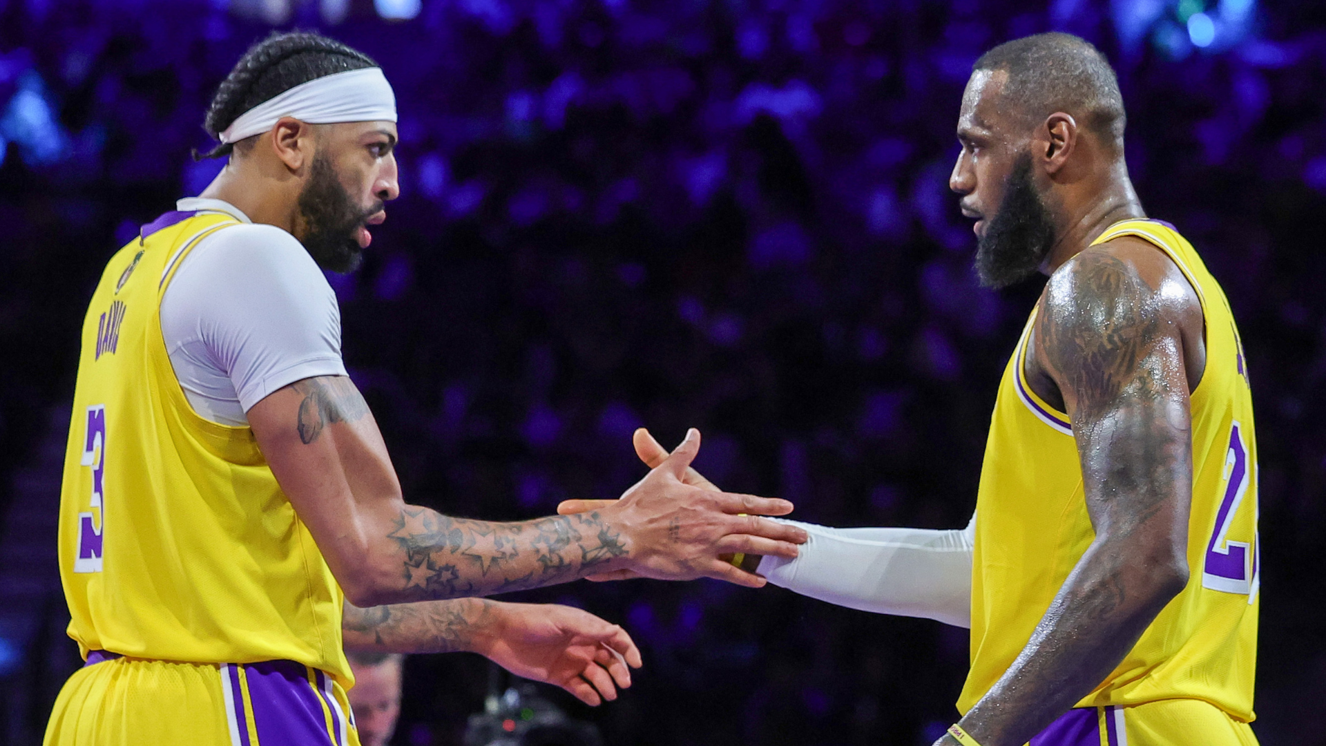Anthony Davis and LeBron James in yellow Lakers jerseys, shaking hands on the basketball court.