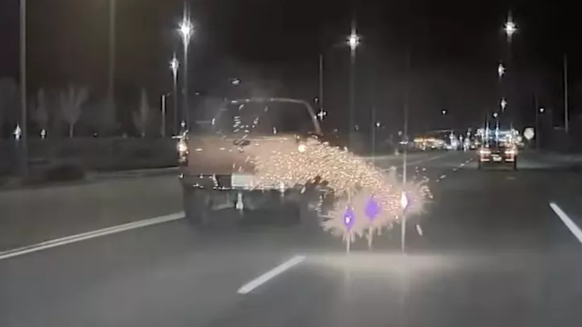 A car driving at night with sparks flying from underneath, possibly due to a mechanical issue. Streetlights illuminate the road.