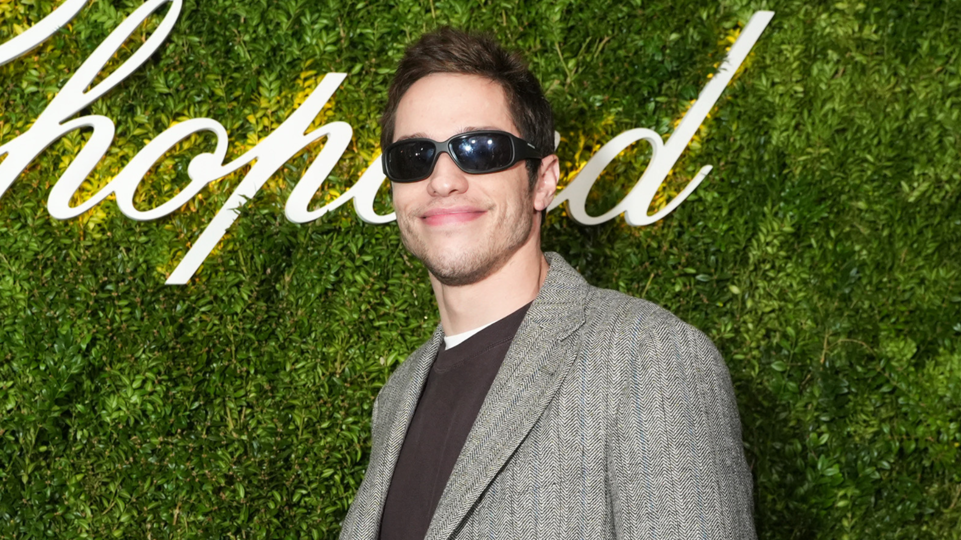 A man in sunglasses and a gray blazer stands in front of a green backdrop with "Chopard" written on it.