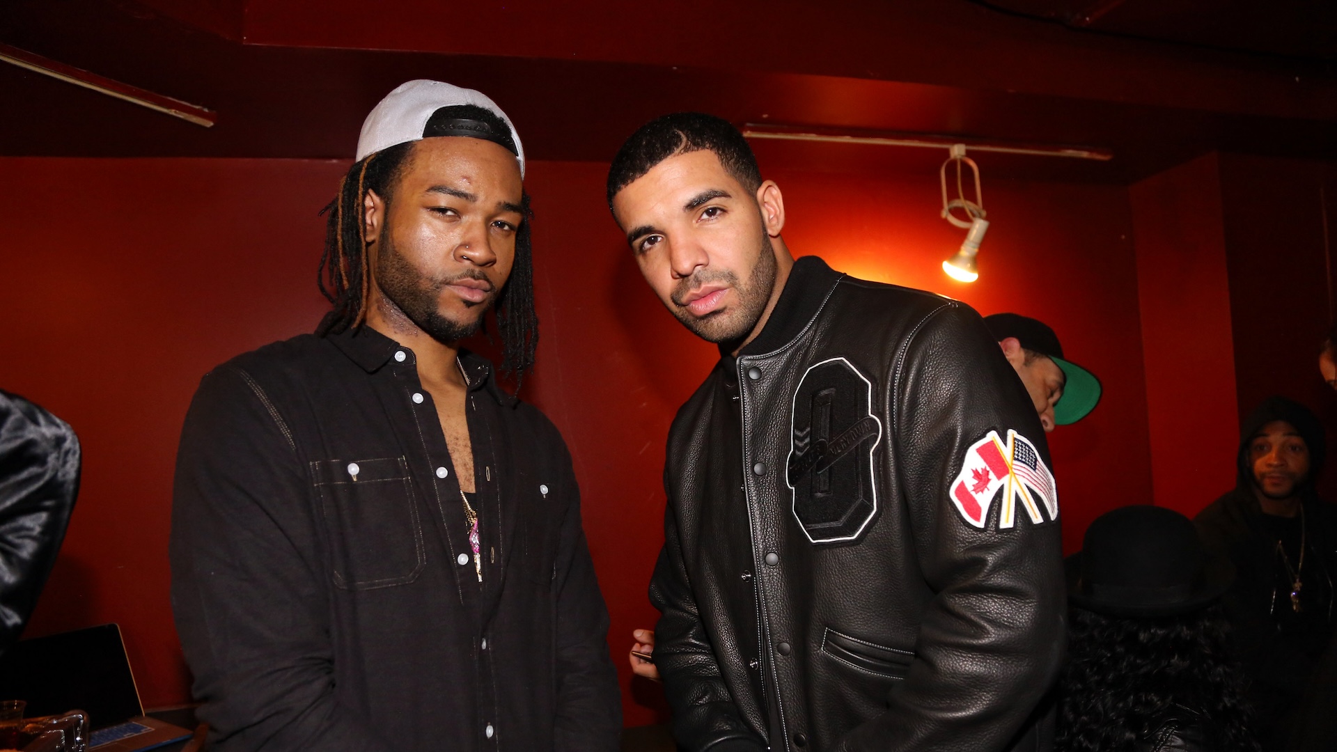 PARTYNEXTDOOR and Drake posing together in a dimly lit room, with red walls and casual attire.