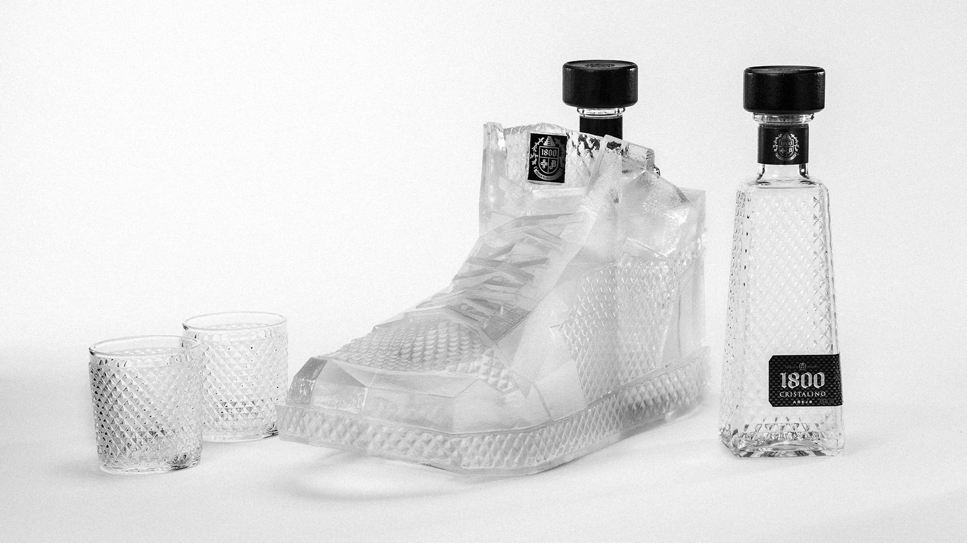 Crystal sneaker-shaped bottle, two glasses, and a bottle of 1800 tequila on a white background.