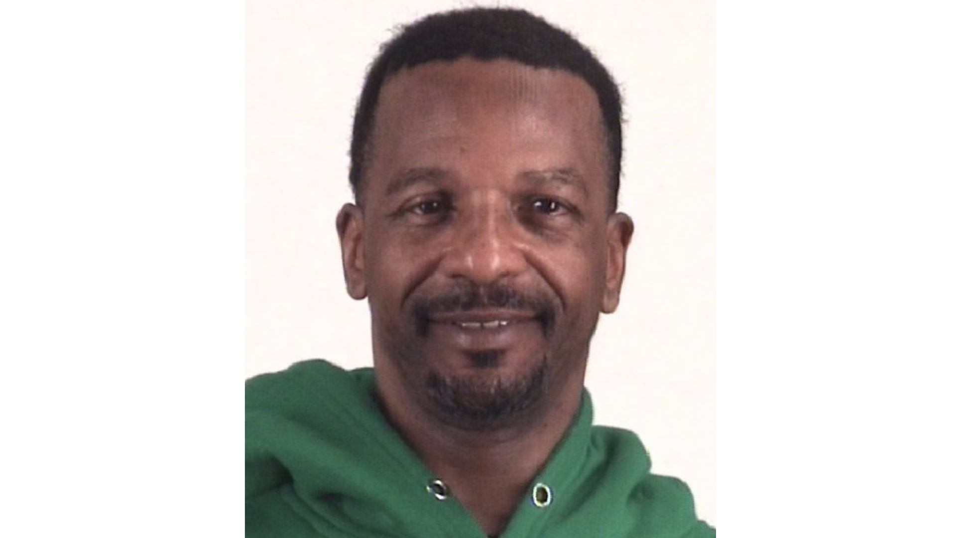 A person wearing a green hoodie, smiling at the camera against a plain background.