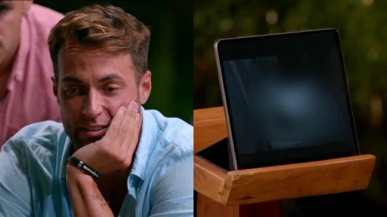 "Temptation Island" star José Carlos Montoya in a blue shirt looking at a tablet on a stand, displaying a black-and-white image.