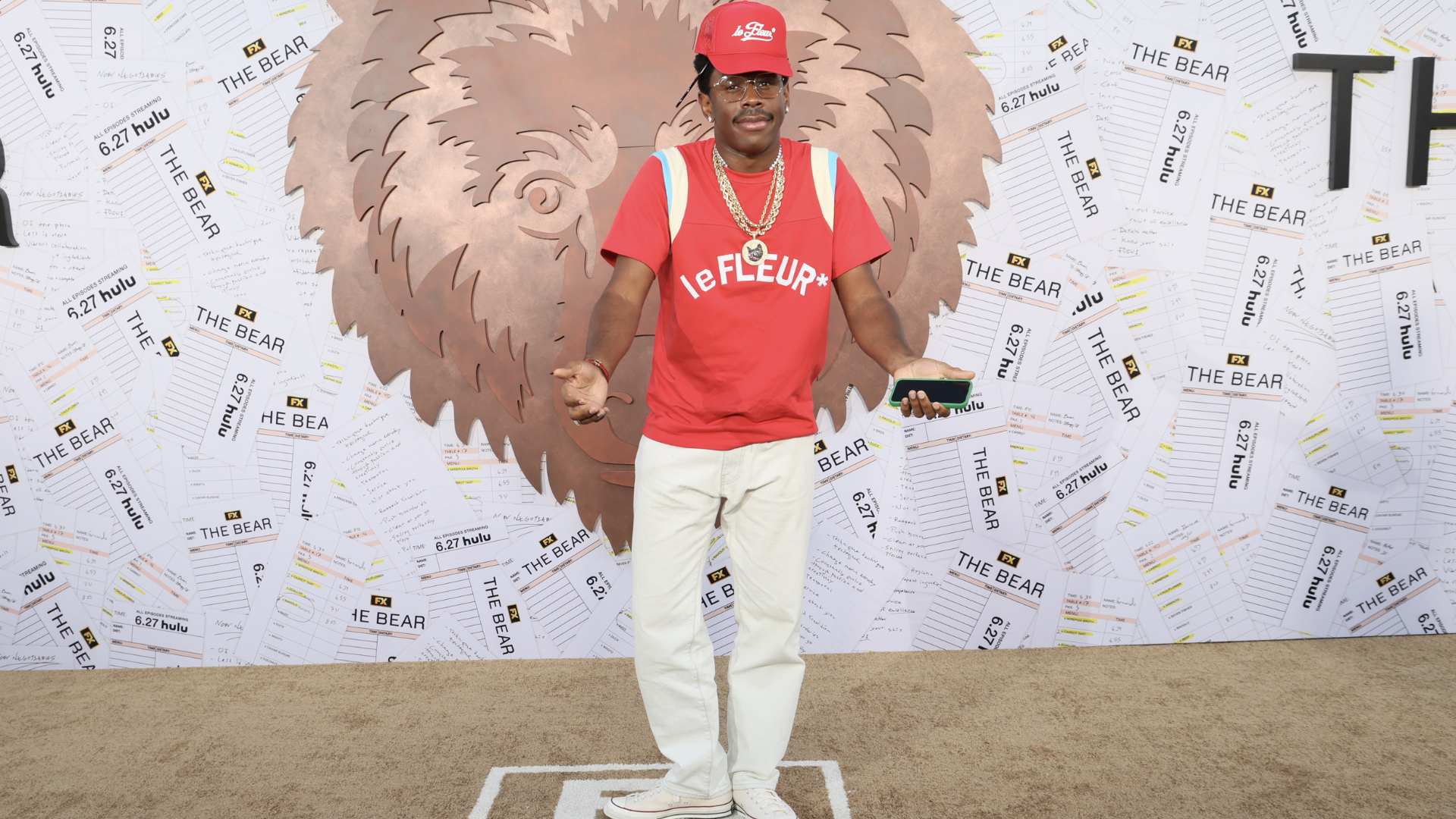 A person wearing a red "le FLEUR" shirt and cap, standing in front of a backdrop with "The Bear" and Hulu logos.