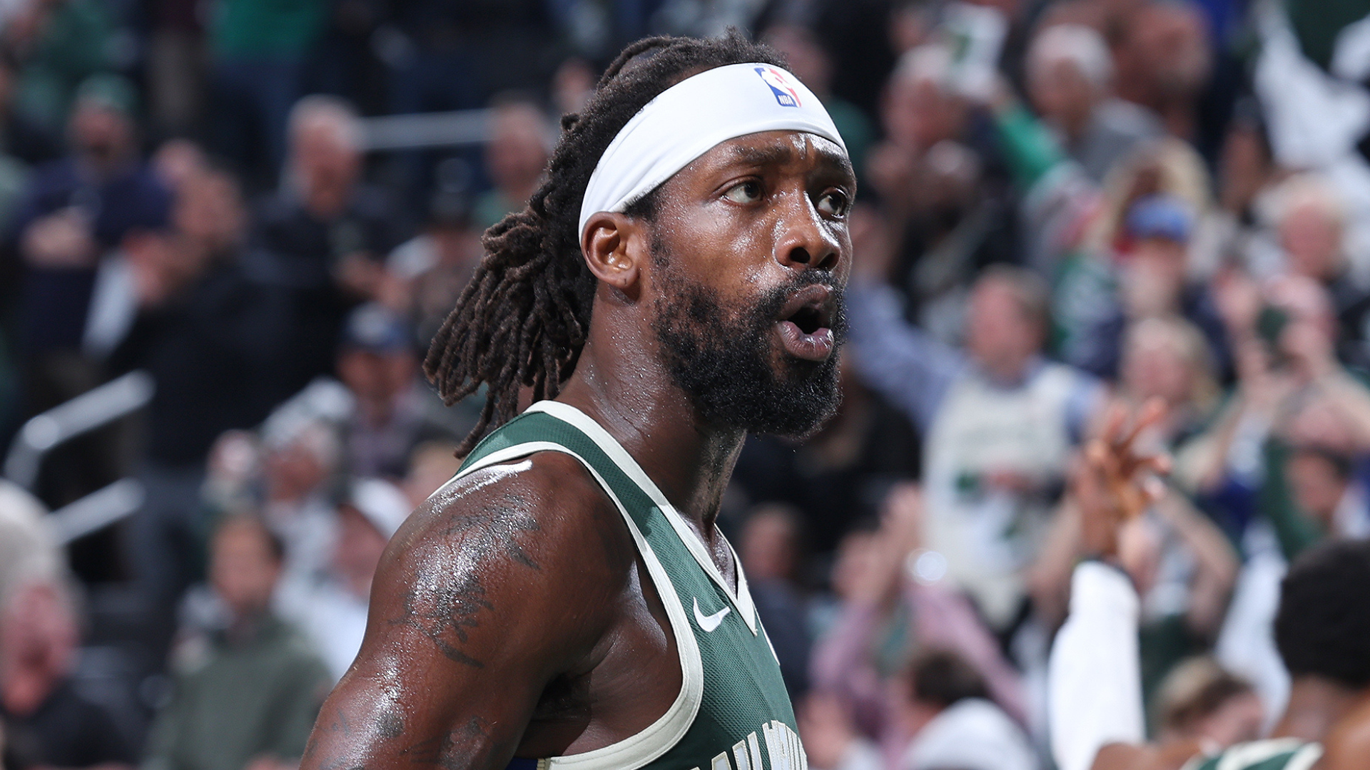 A basketball player with a beard and headband, wearing a green jersey, is on the court with a crowd in the background.