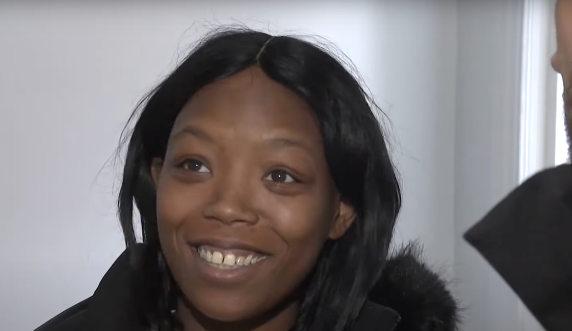 A woman smiling indoors, wearing a black jacket.