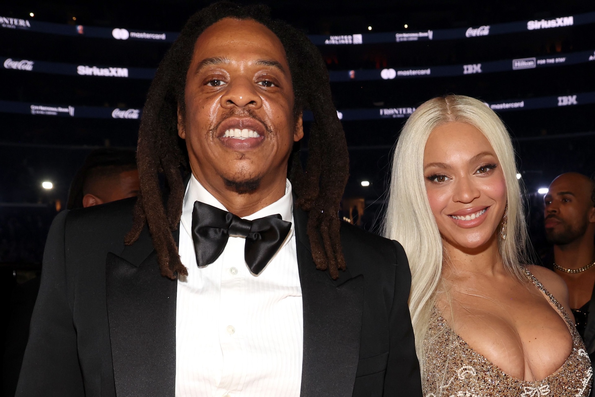 Jay-Z and Beyoncé smiling at an event. Jay-Z is in a tuxedo, and Beyoncé is wearing a sparkling dress.