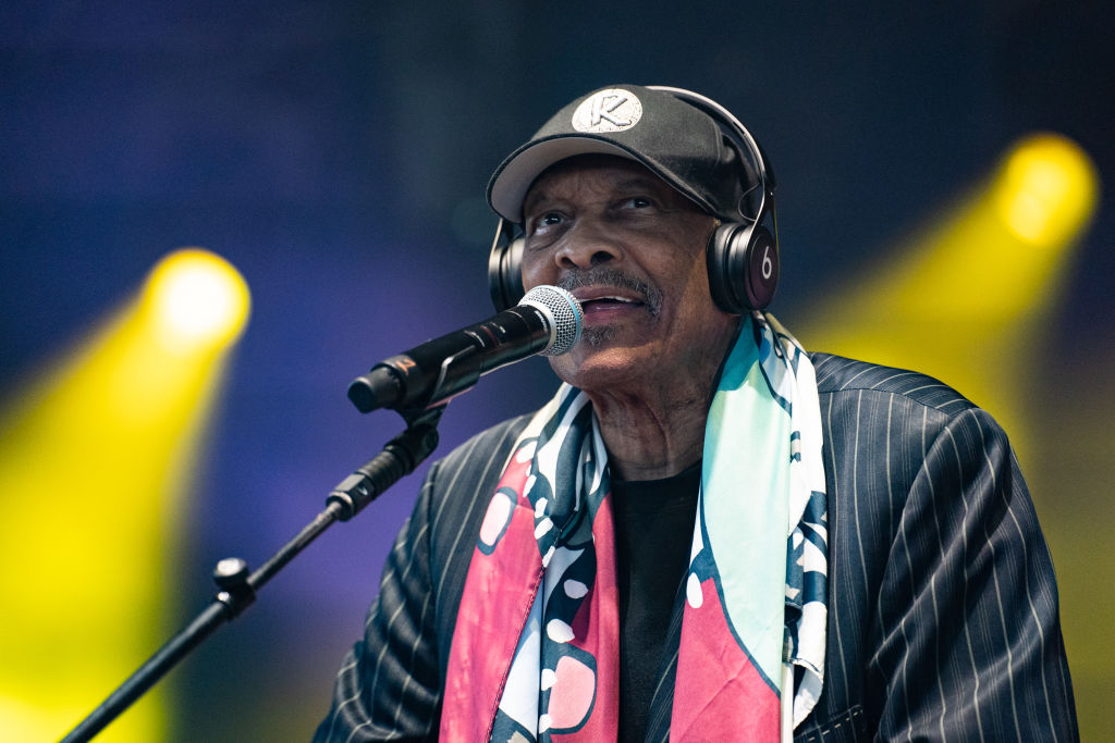 Man wearing headphones and a colorful scarf, performing on stage with a microphone, under bright stage lights.