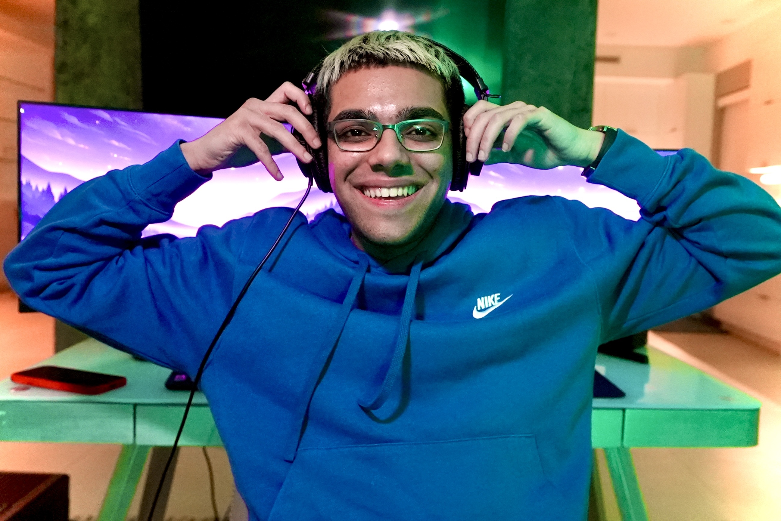 Mikyle Rafiq, also known by his streamer name N3on, in a blue Nike hoodie smiling and wearing headphones, sitting in front of a glowing computer screen.