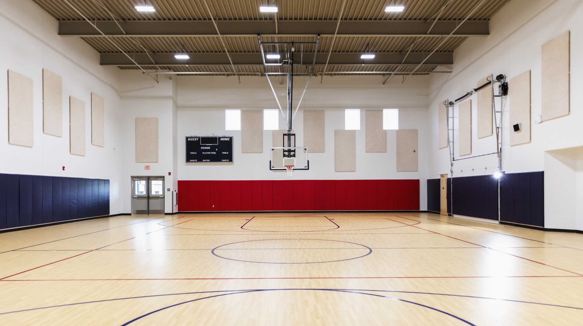 An empty school gymnasium with a basketball court. In the background are a scoreboard and the basketball hoop.