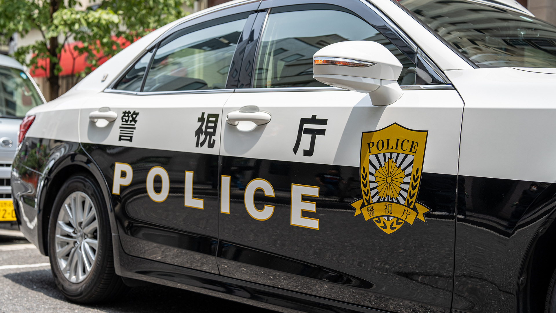 A Japanese police car with black and white design, featuring the word "POLICE" and Japanese characters on the side, parked on a street.