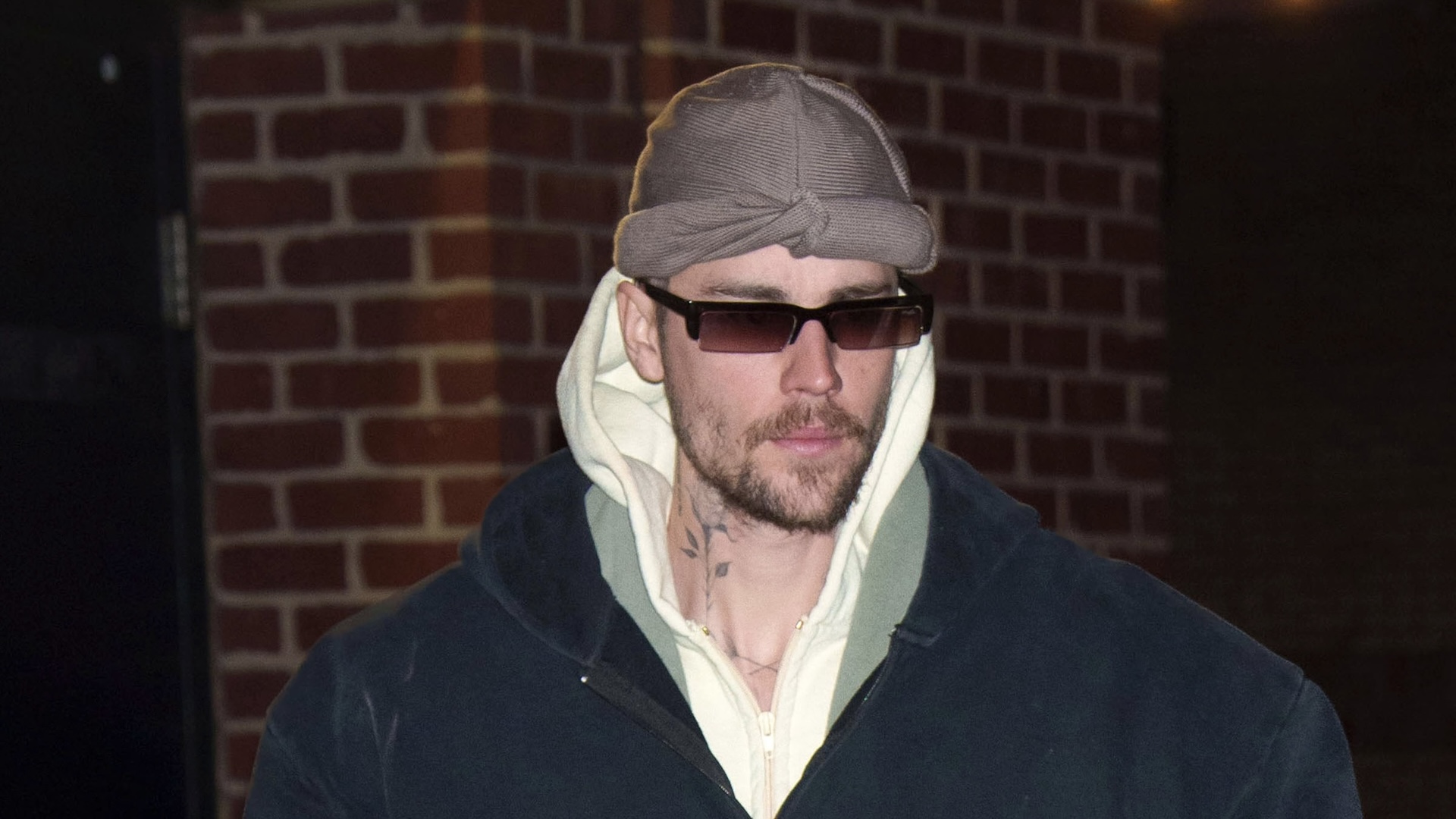 Justin Bieber wearing a blue hoodie, sunglasses, and a gray hat.