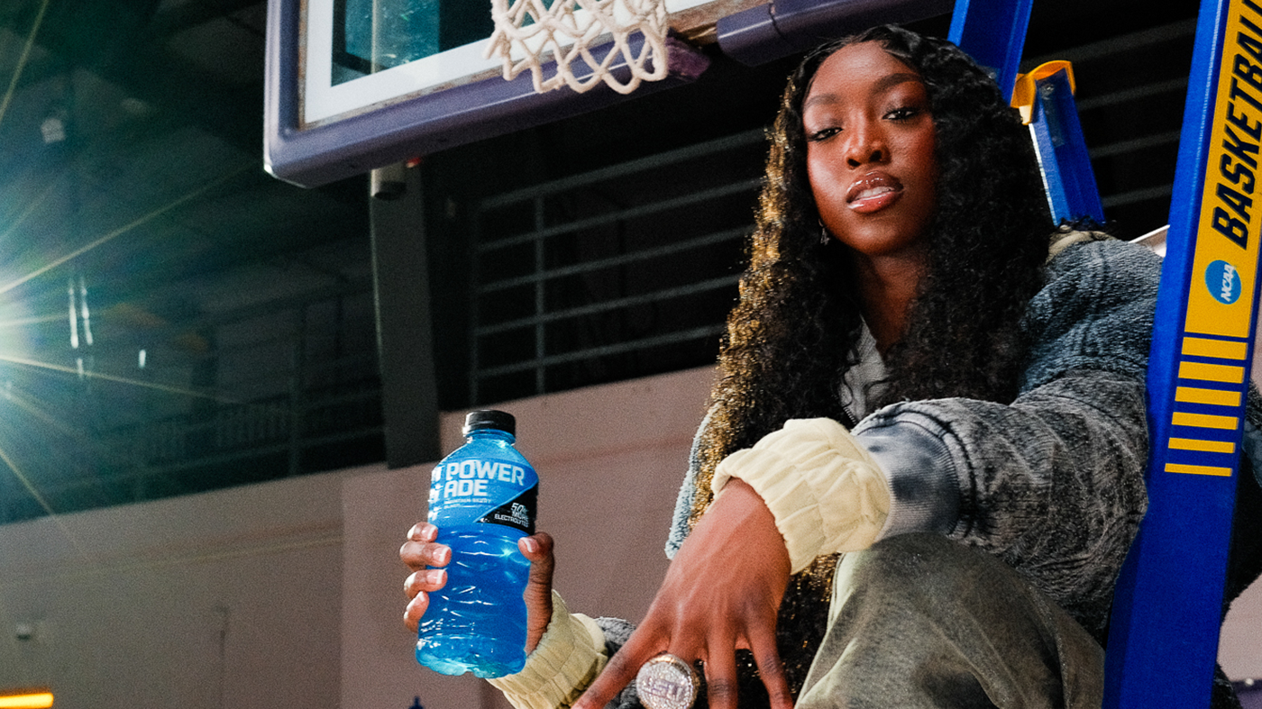 Flau'Jae Johnson sits on a ladder in a basketball court, holding a blue Powerade bottle.