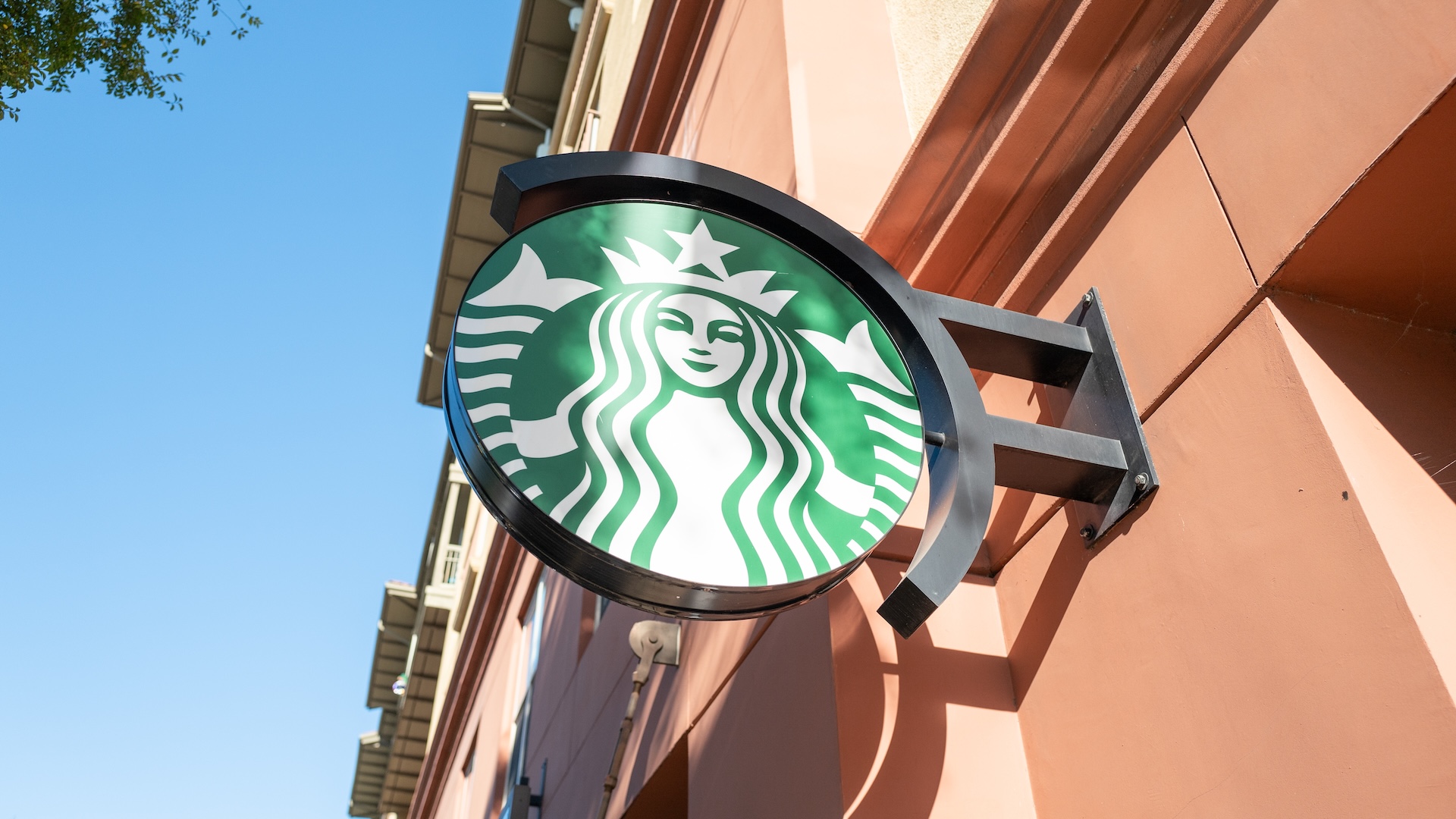 Starbucks logo sign on the exterior of a building, featuring the iconic green and white mermaid design.