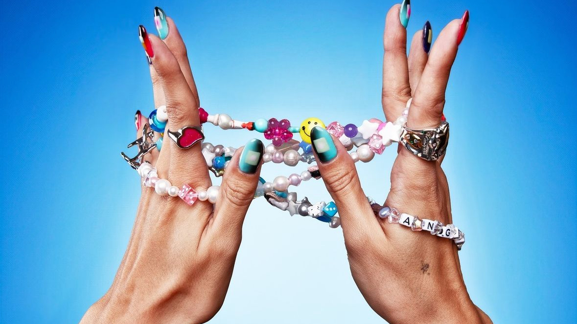 Hands with colorful, beaded bracelets and rings, featuring letters and smiley faces, against a blue background. Jewelry from Ian Charms now available on complex shop